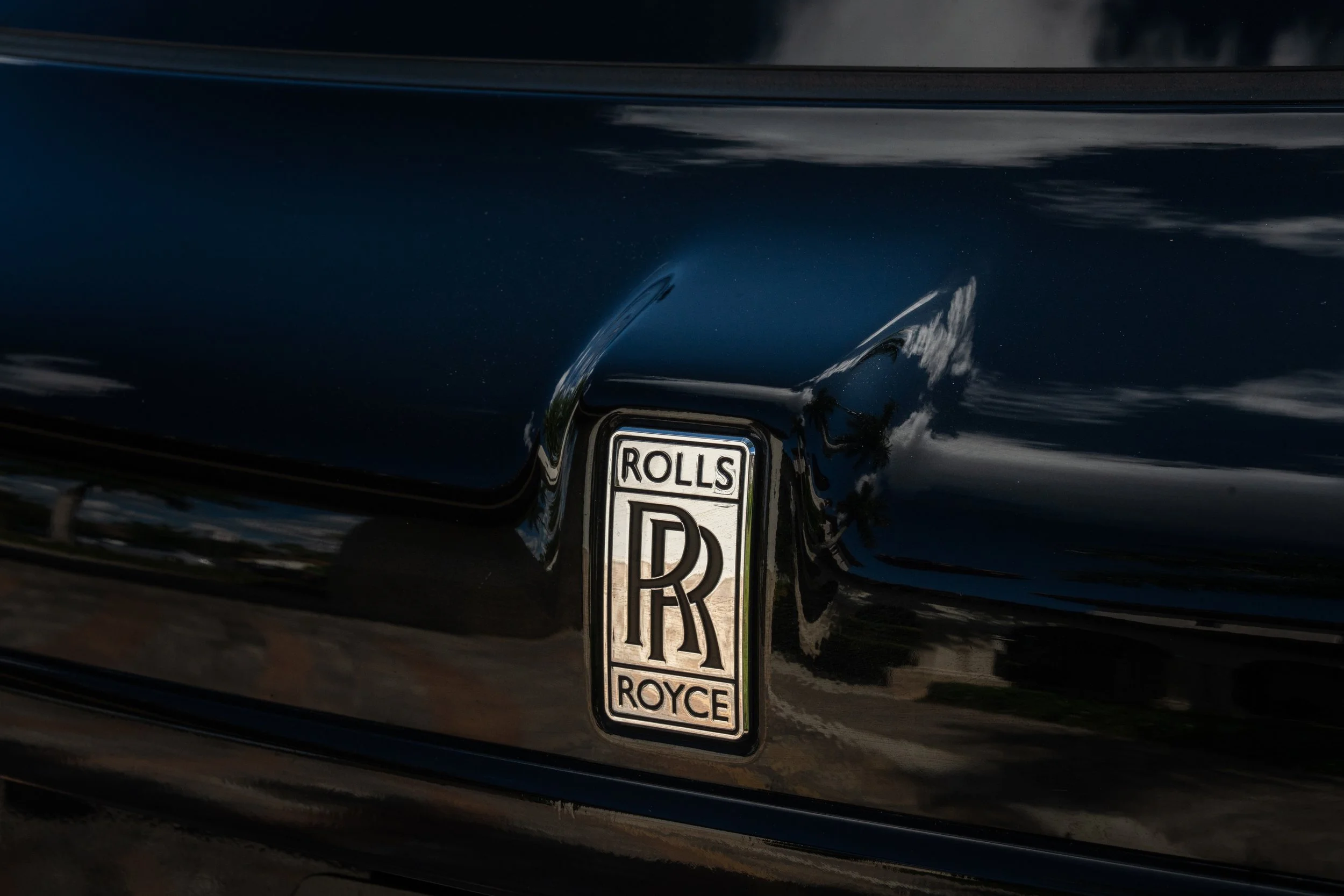 Close-up of a black luxury car with a silver Rolls-Royce emblem on the trunk.