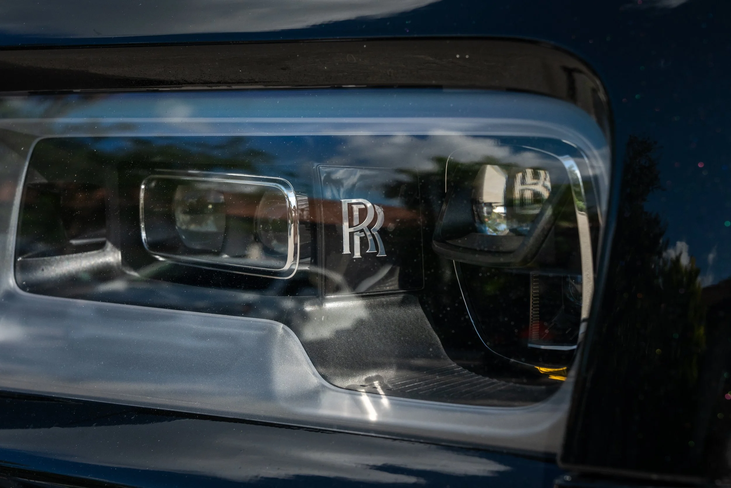 Close-up of a Rolls-Royce car's headlight with the Rolls-Royce logo visible inside.
