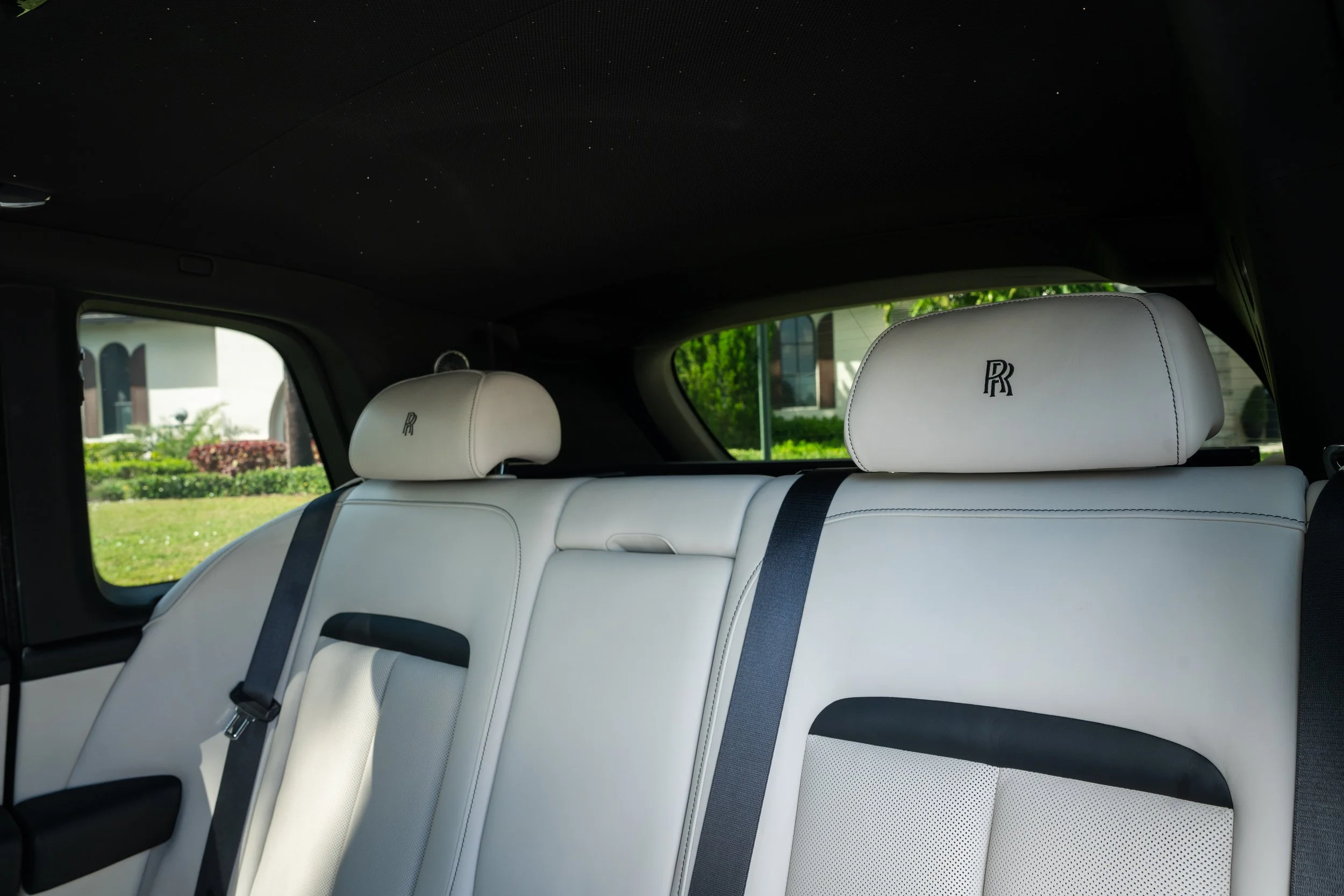 Inside the rear seats of a luxury vehicle with white leather upholstery and Rolls-Royce logos on the headrests.