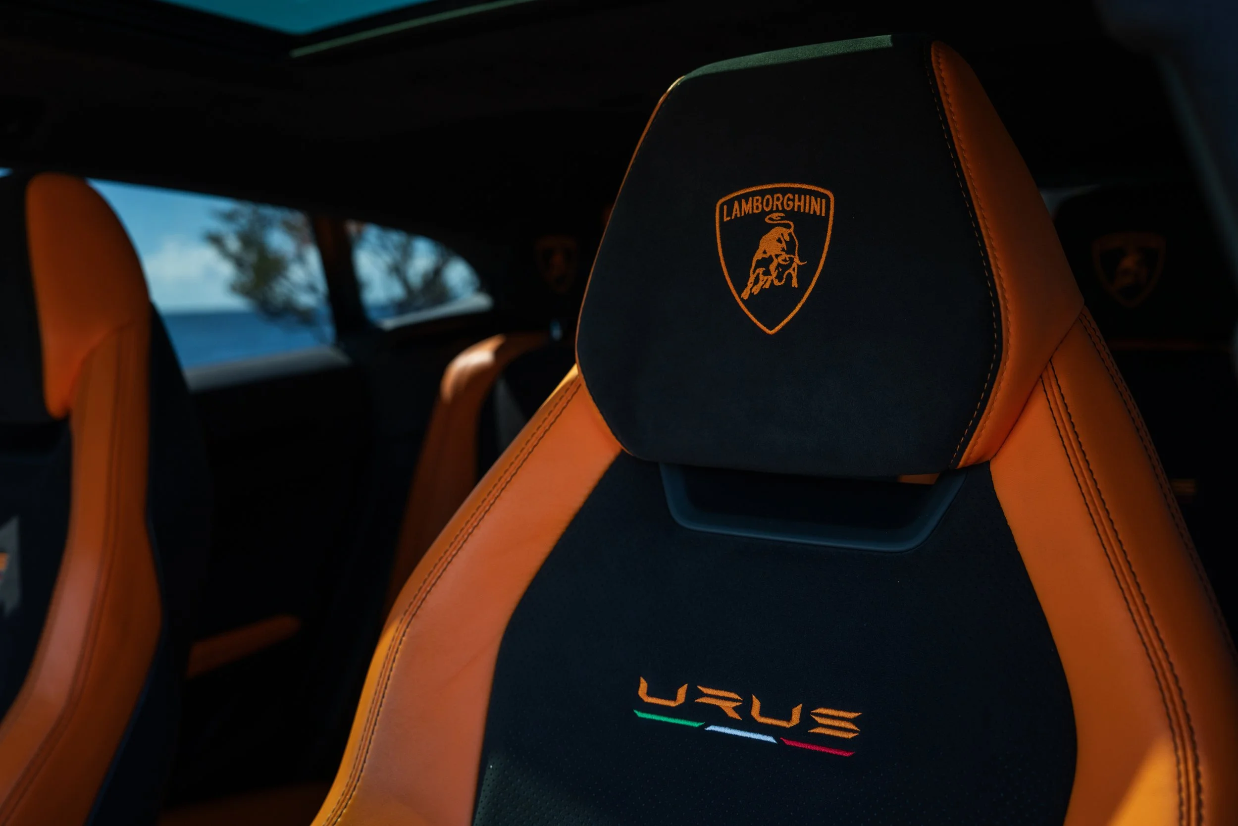 Close-up of black and orange Lamborghini Urus car seat with Lamborghini logo on headrest and embroidered 'URUS' text with Italian flag colors