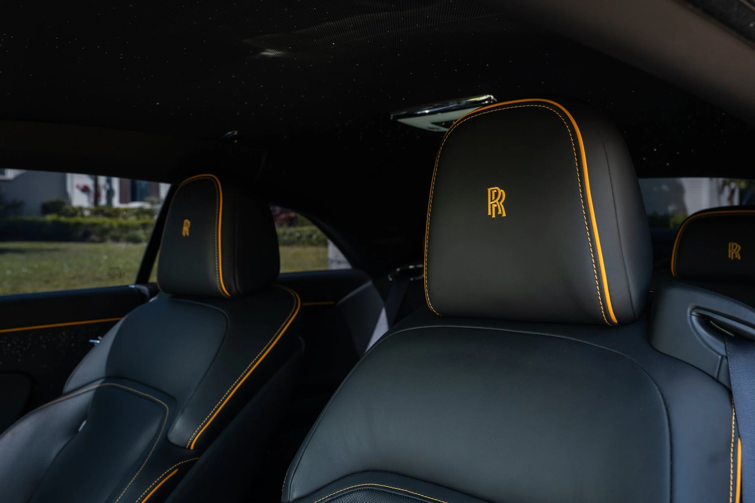 Close-up of luxury car seats with black leather upholstery and golden yellow stitching, featuring embroidered 'RR' logos on the headrests.