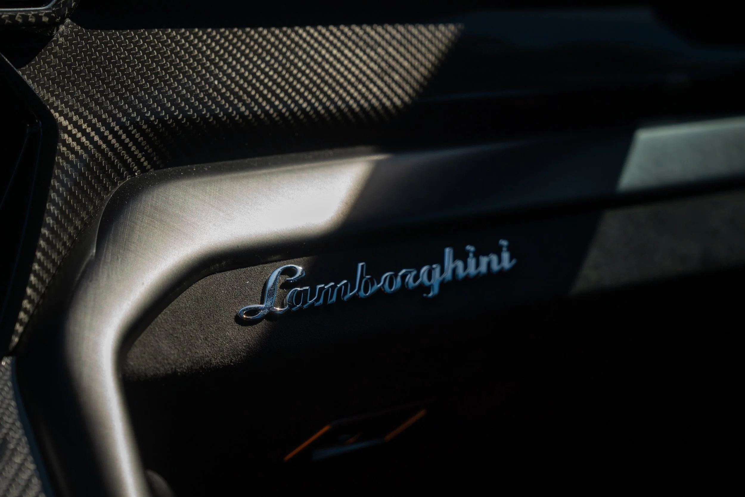 Close-up of Lamborghini logo on the dashboard of a car with carbon fiber trim.