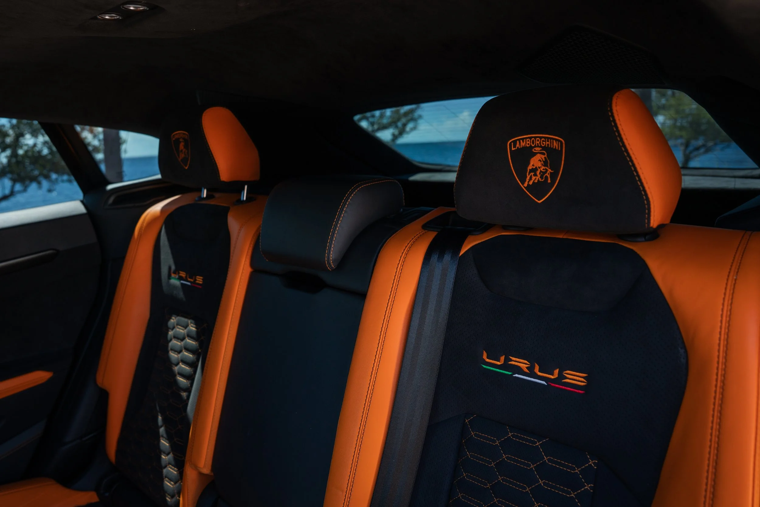 The interior of a Lamborghini Urus SUV, featuring orange and black leather seats with Lamborghini and Urus branding embroidered on the headrests and backrests.