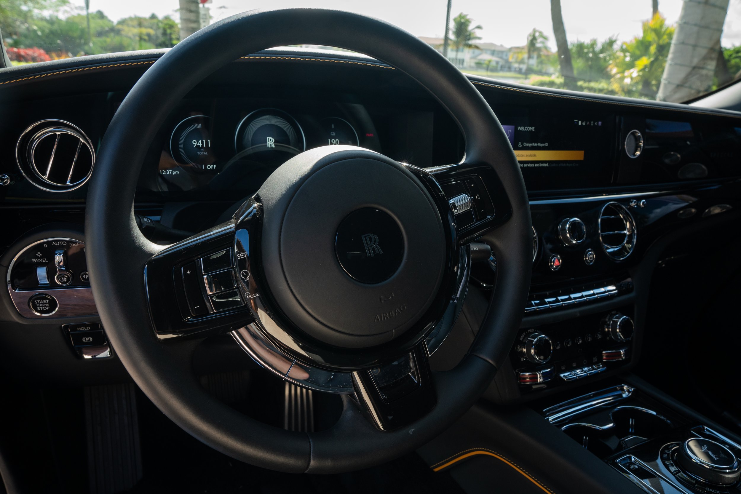 The interior dashboard of a luxury Rolls-Royce car, showing the steering wheel with the iconic Rolls-Royce logo, digital instrument cluster, and central control panel with various dials and buttons.