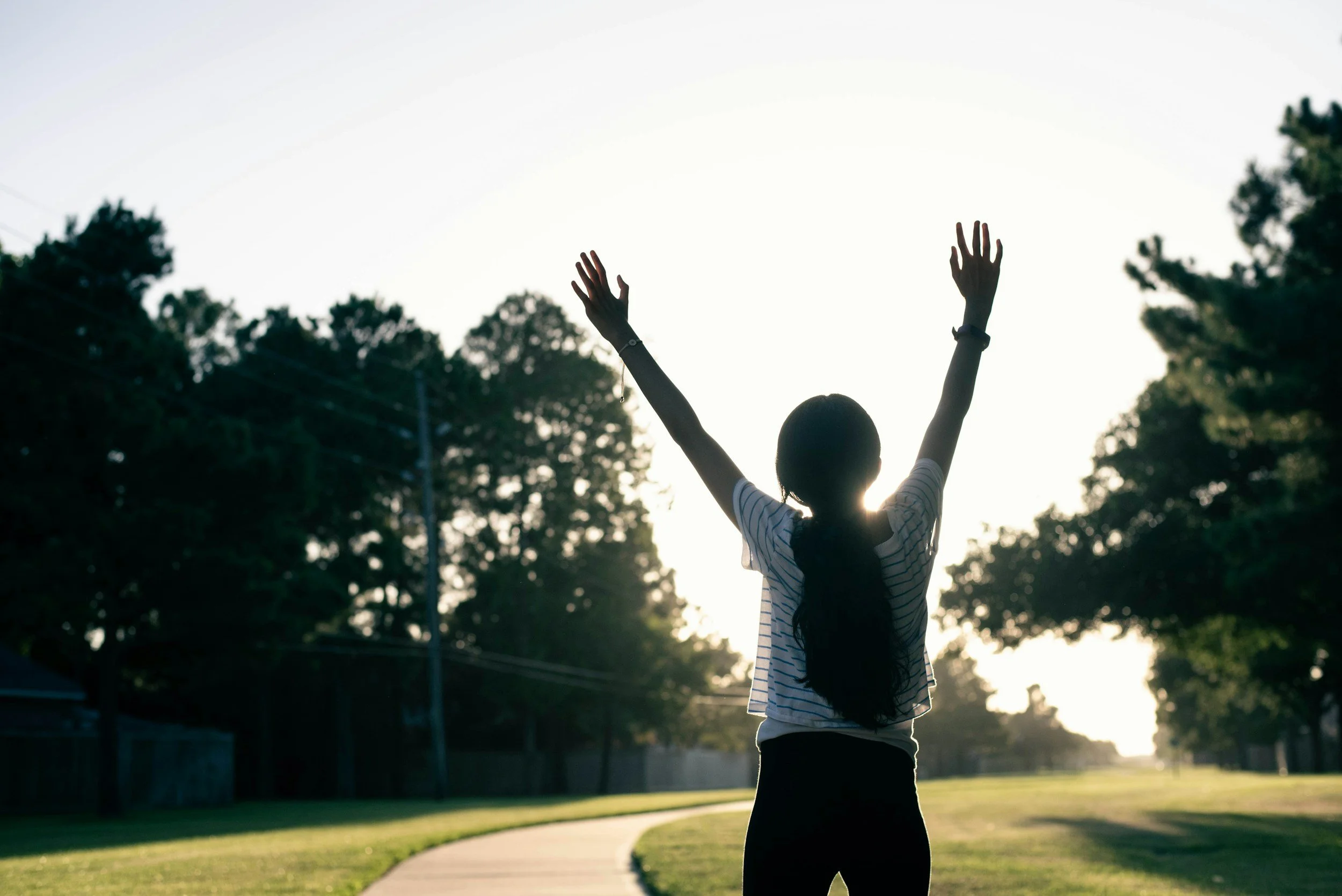 Young Asian American female, with her hands raised up in a park in Albany, CA to celebrate meeting her goals in therapy for estrangement, especially among young adults, Asian Americans, and caregivers through online and in-person therapy services
