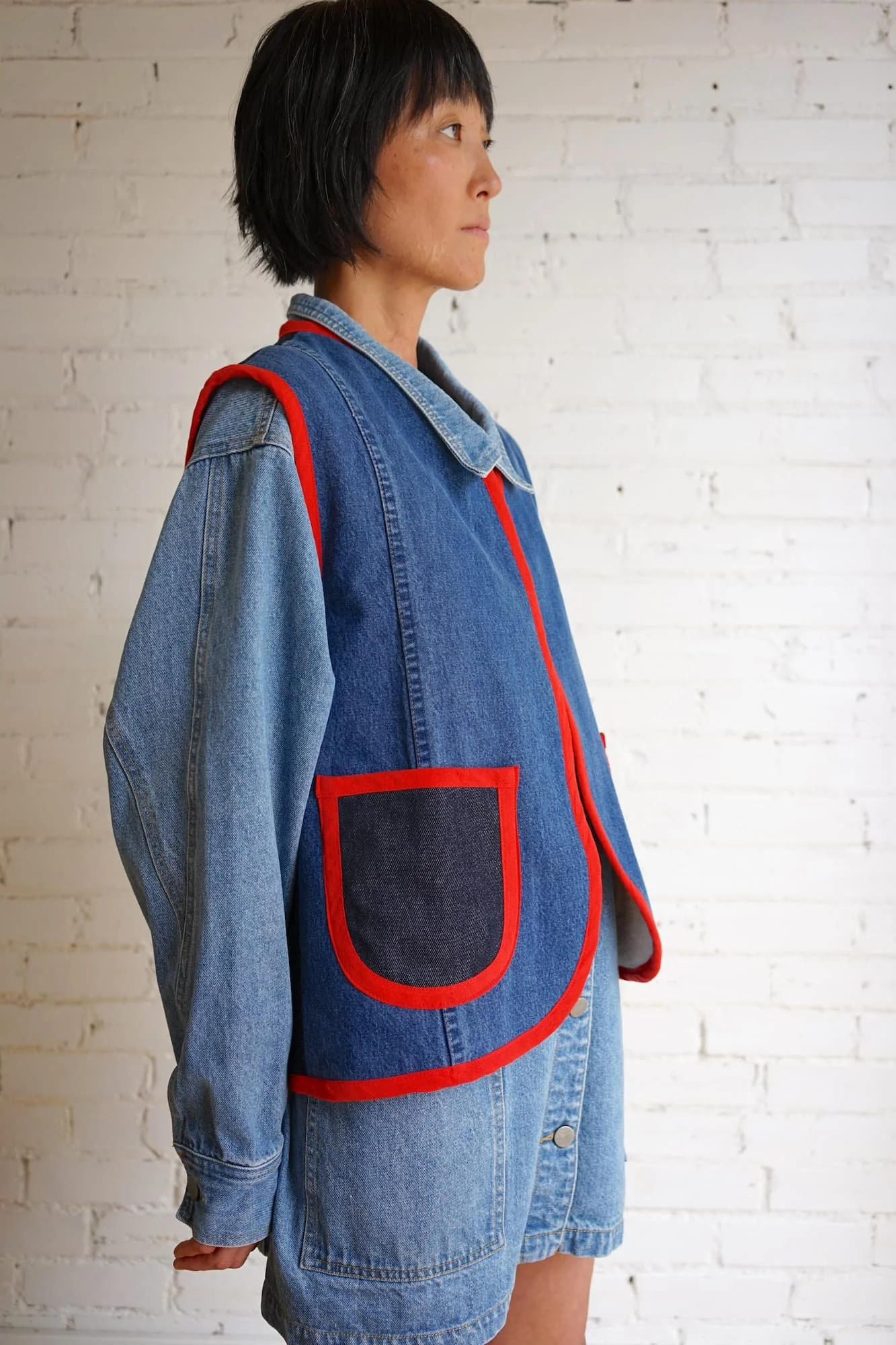 Woman wearing repurposed denim Nomad Utility Vest with red binding over a denim jacket