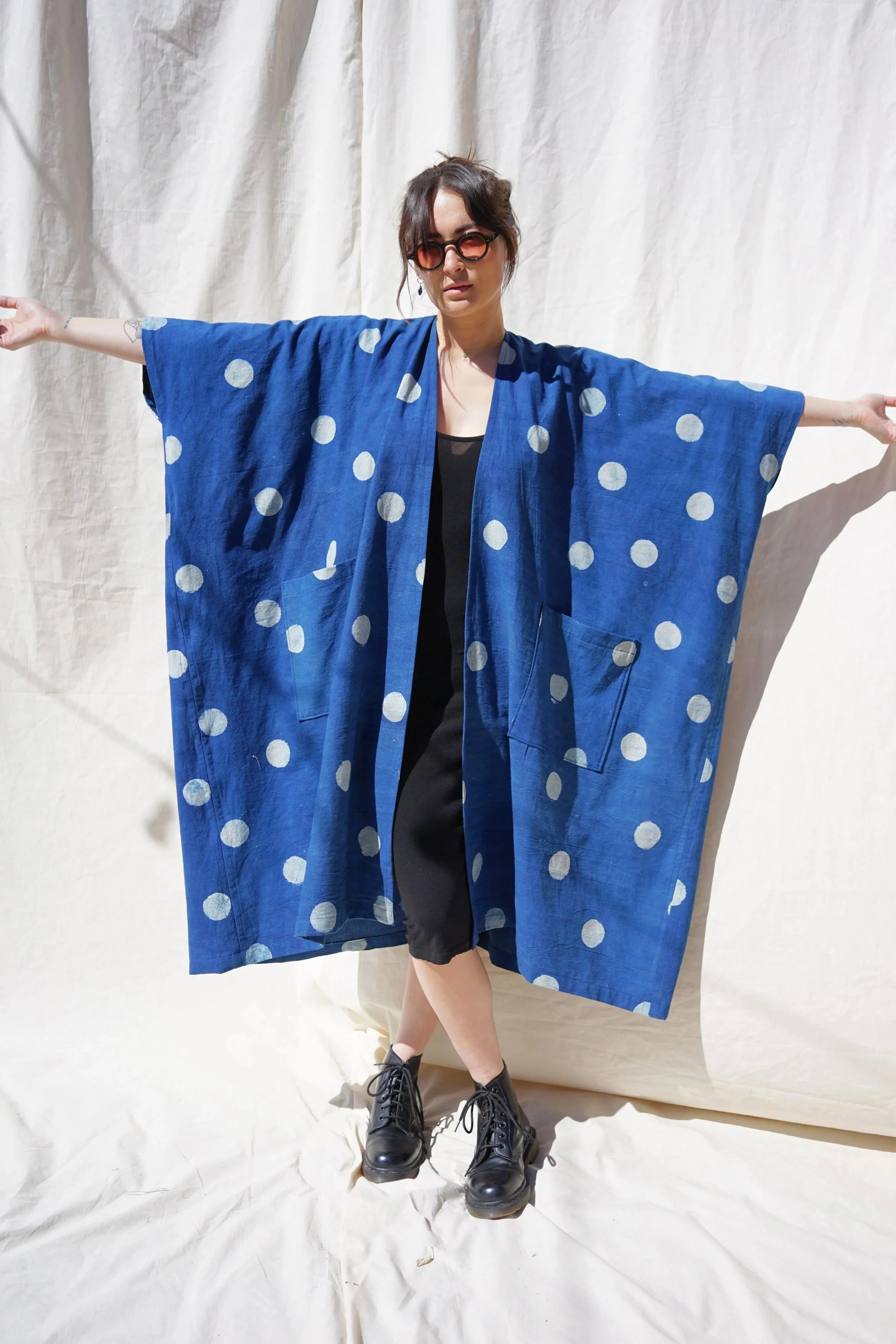 Model wearing the long kimono cover-up in indigo blue cotton with hand-printed white polka dots, arms extended wide showing sleeve drape, front view