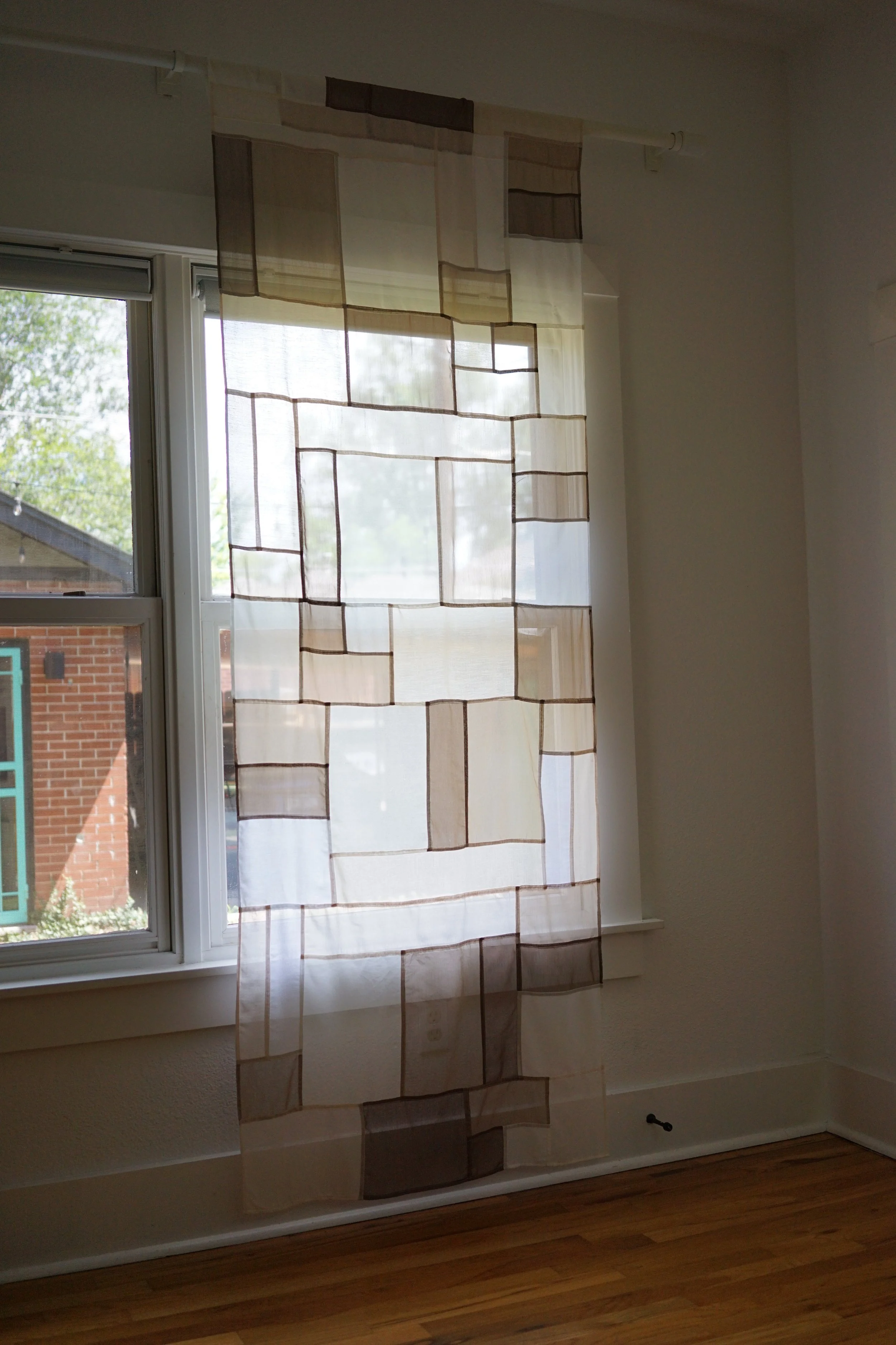 Neutral jogakbo patchwork curtain hanging in front of window in sunlit room