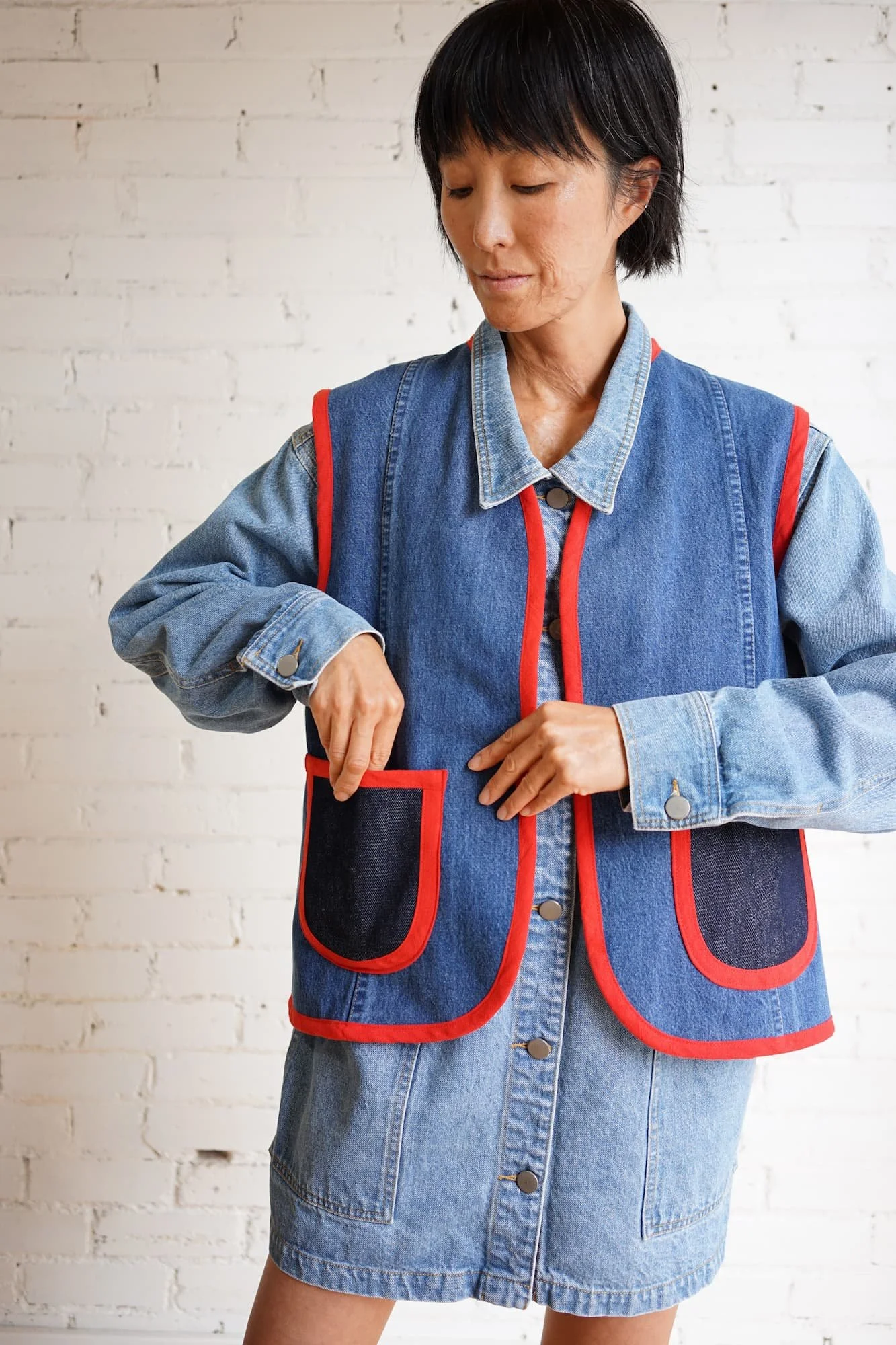 Close-up of woman reaching into patch pocket of indigo denim Nomad Utility Vest with red binding