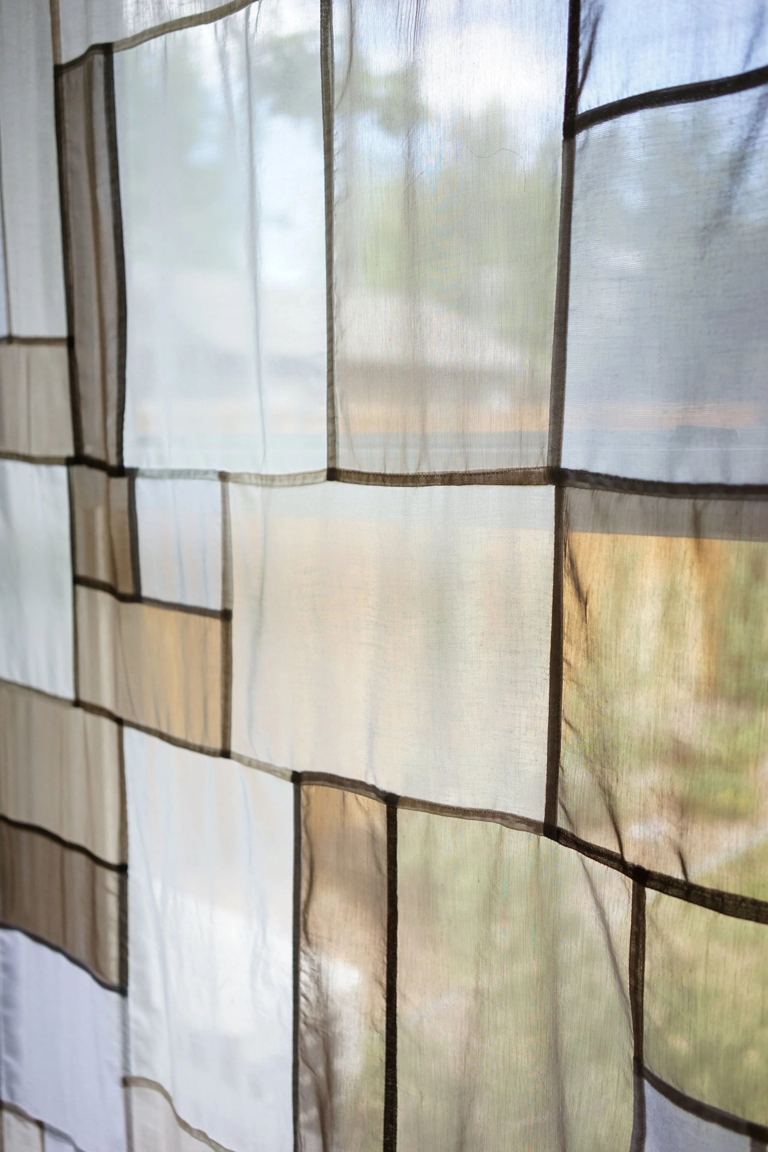 Close-up of jogakbo patchwork curtain against window, showing sheer fabric panels with dark stitched seams