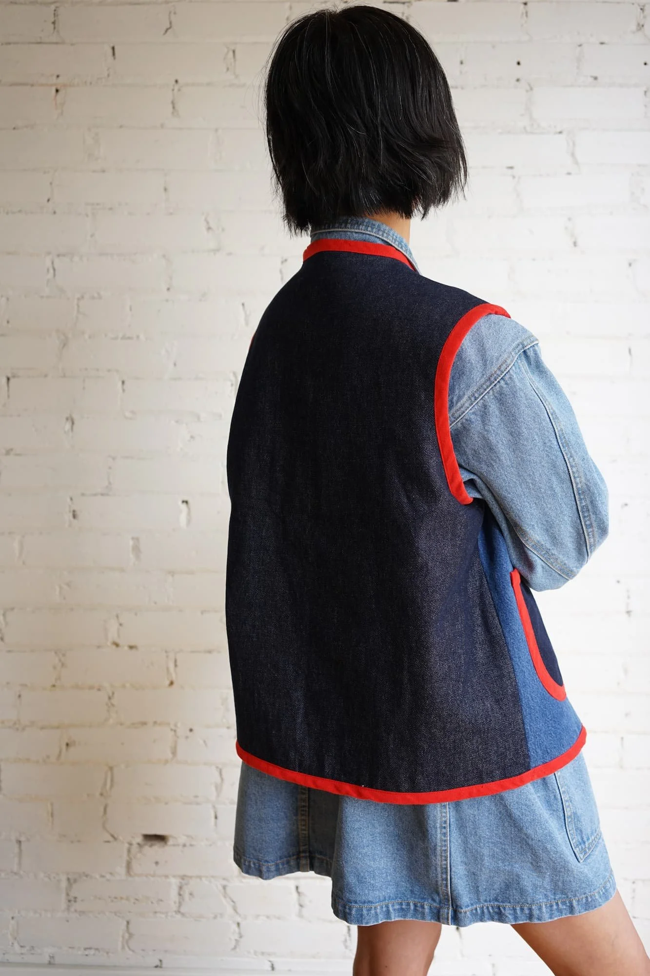Back view of indigo denim Nomad Utility Vest with red binding, worn over a denim jacket