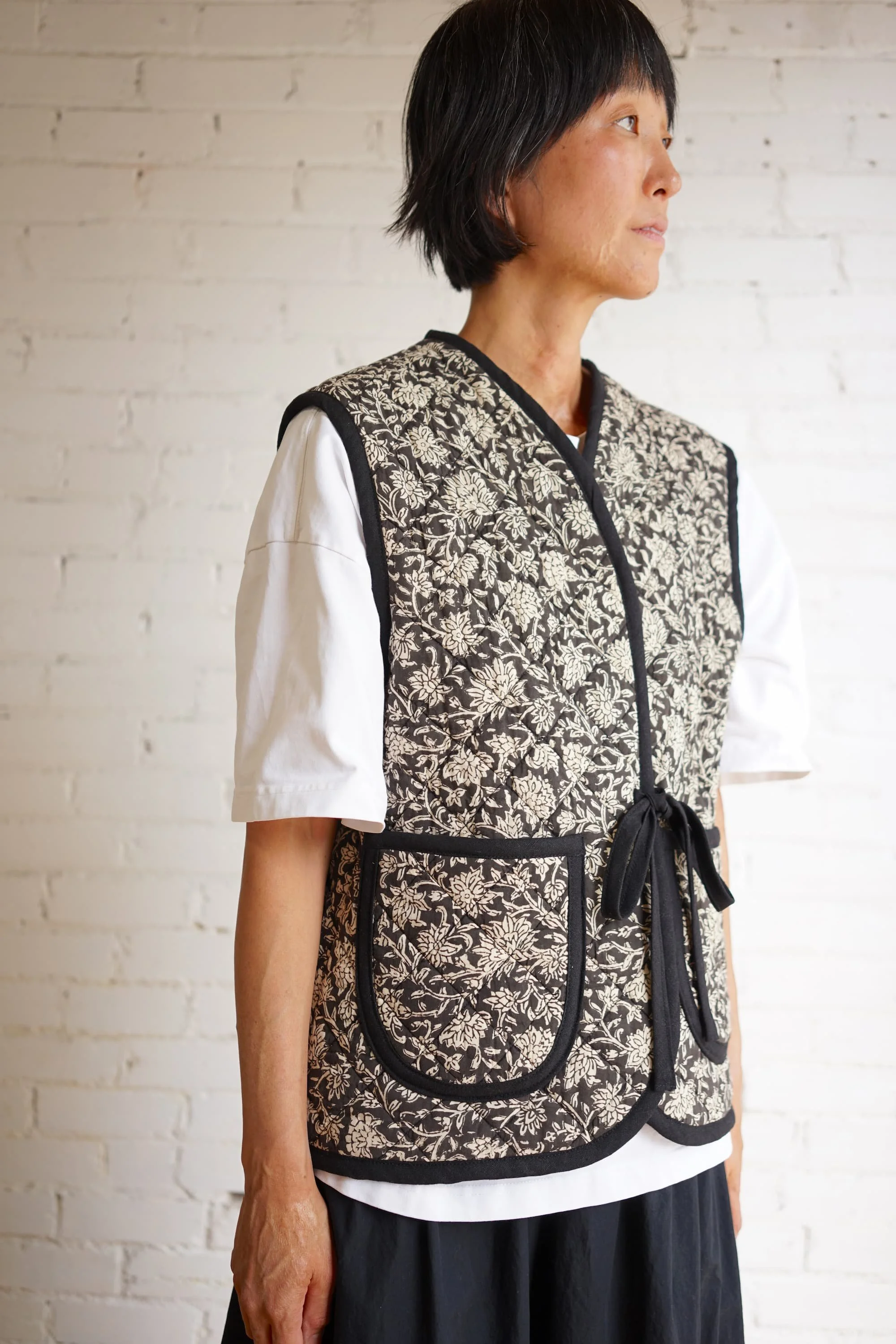 Side view of block-print quilted Nomad Utility Vest in black and cream floral pattern with black binding