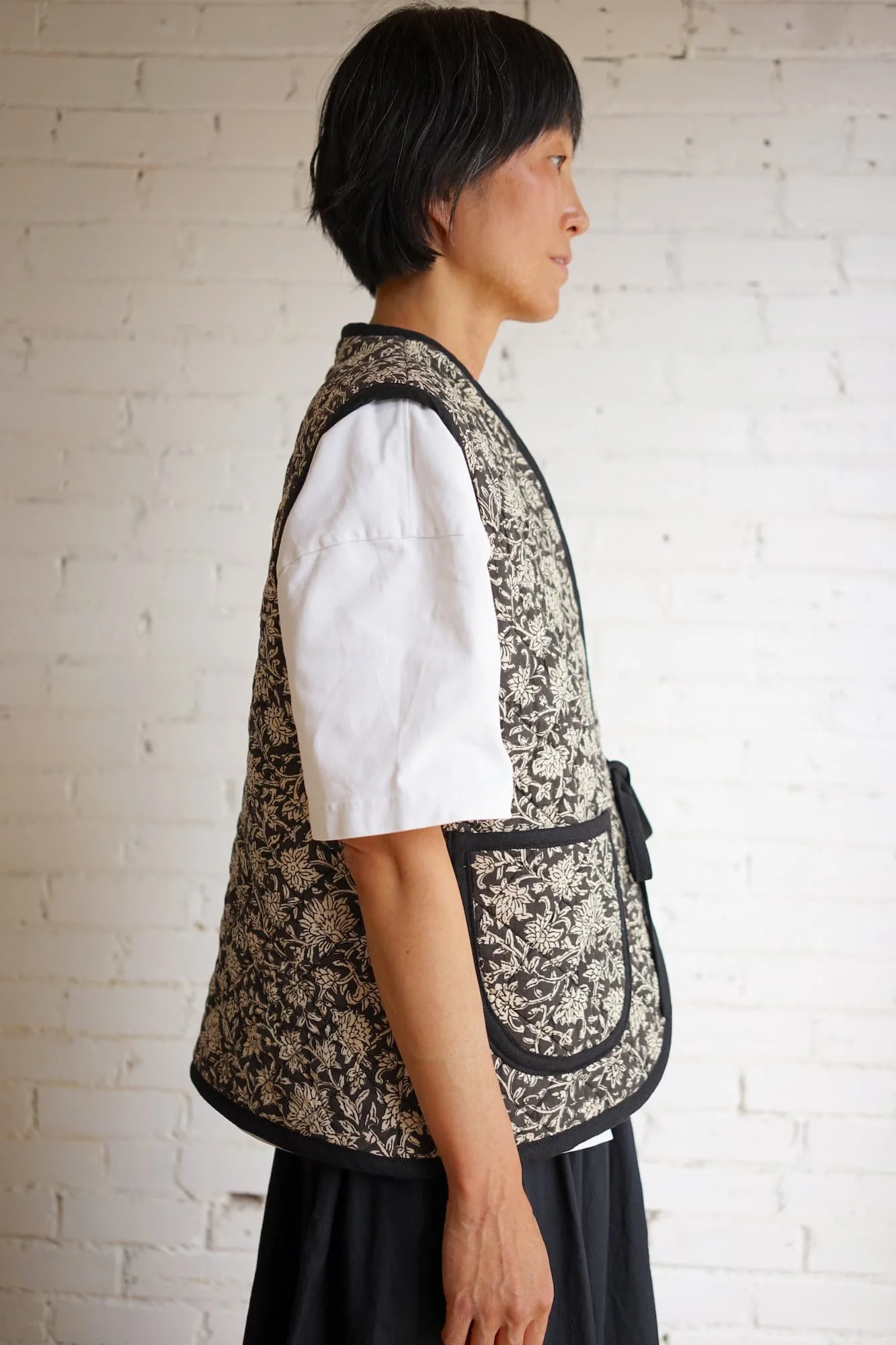 Side profile of block-print quilted Nomad Utility Vest in black and cream floral pattern with tie closure