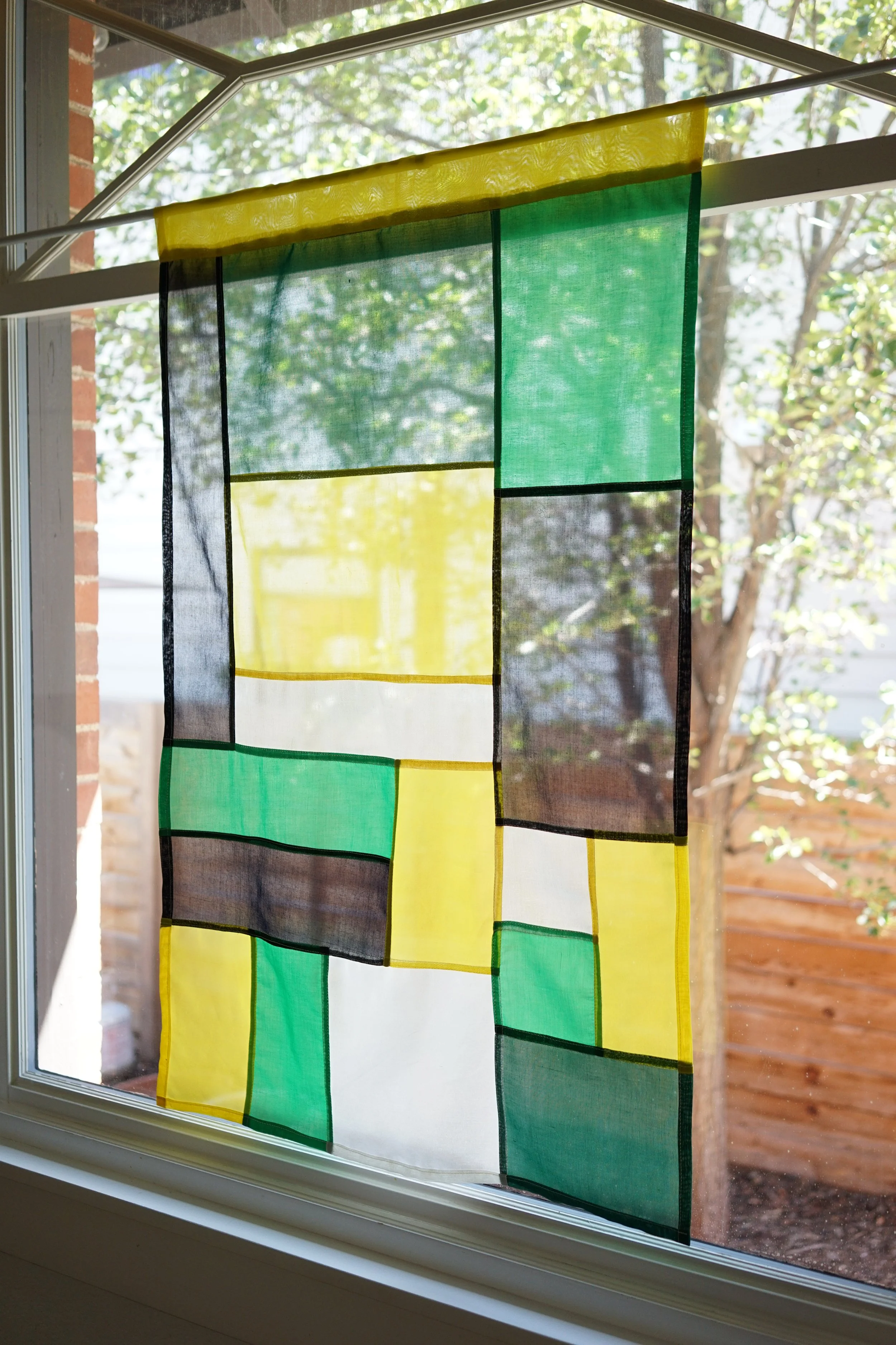 Citrine jogakbo window hanging in window against brick exterior and trees