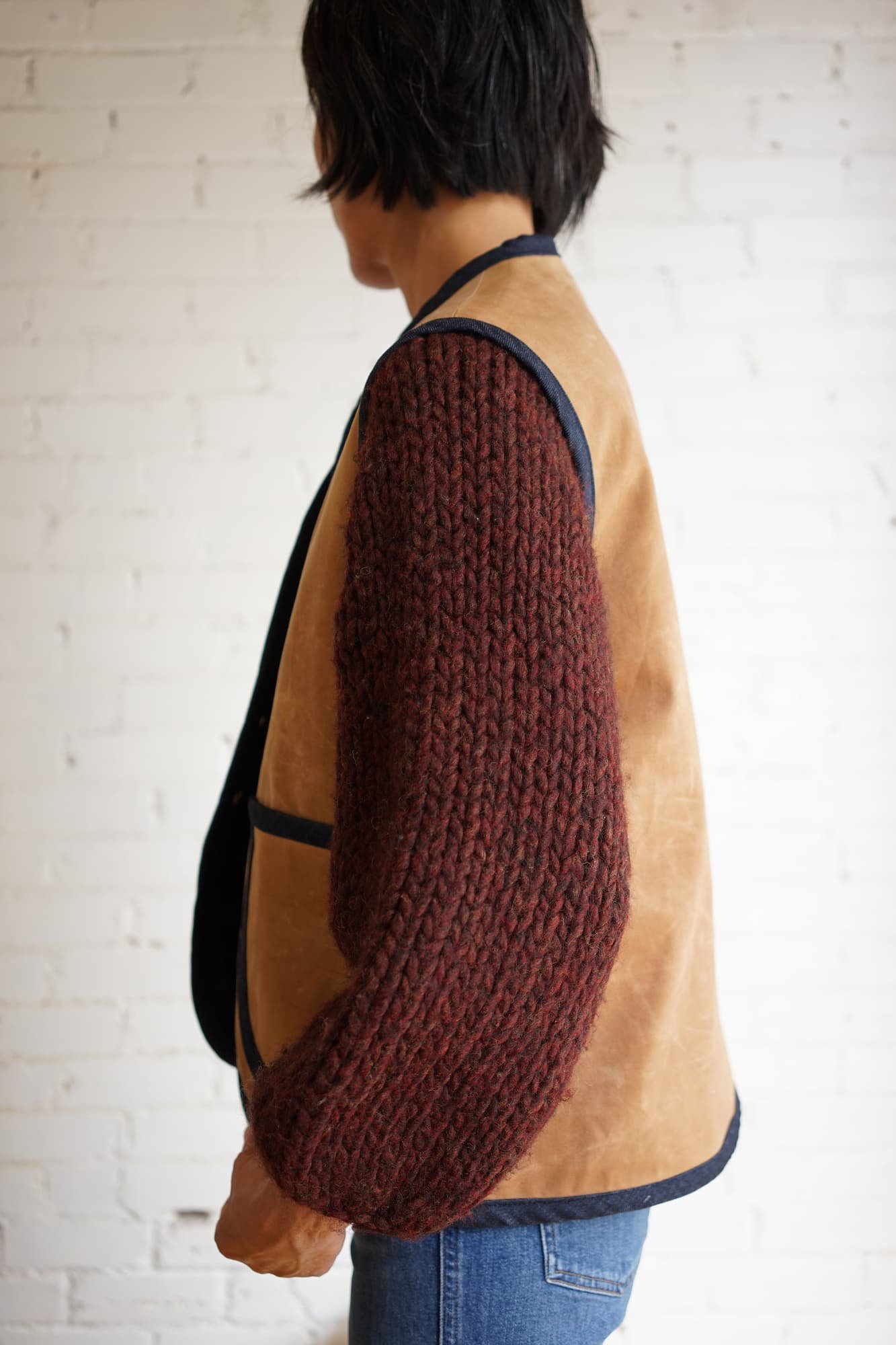 Side view of tan waxed canvas Nomad Utility Vest worn over a burgundy knit sweater