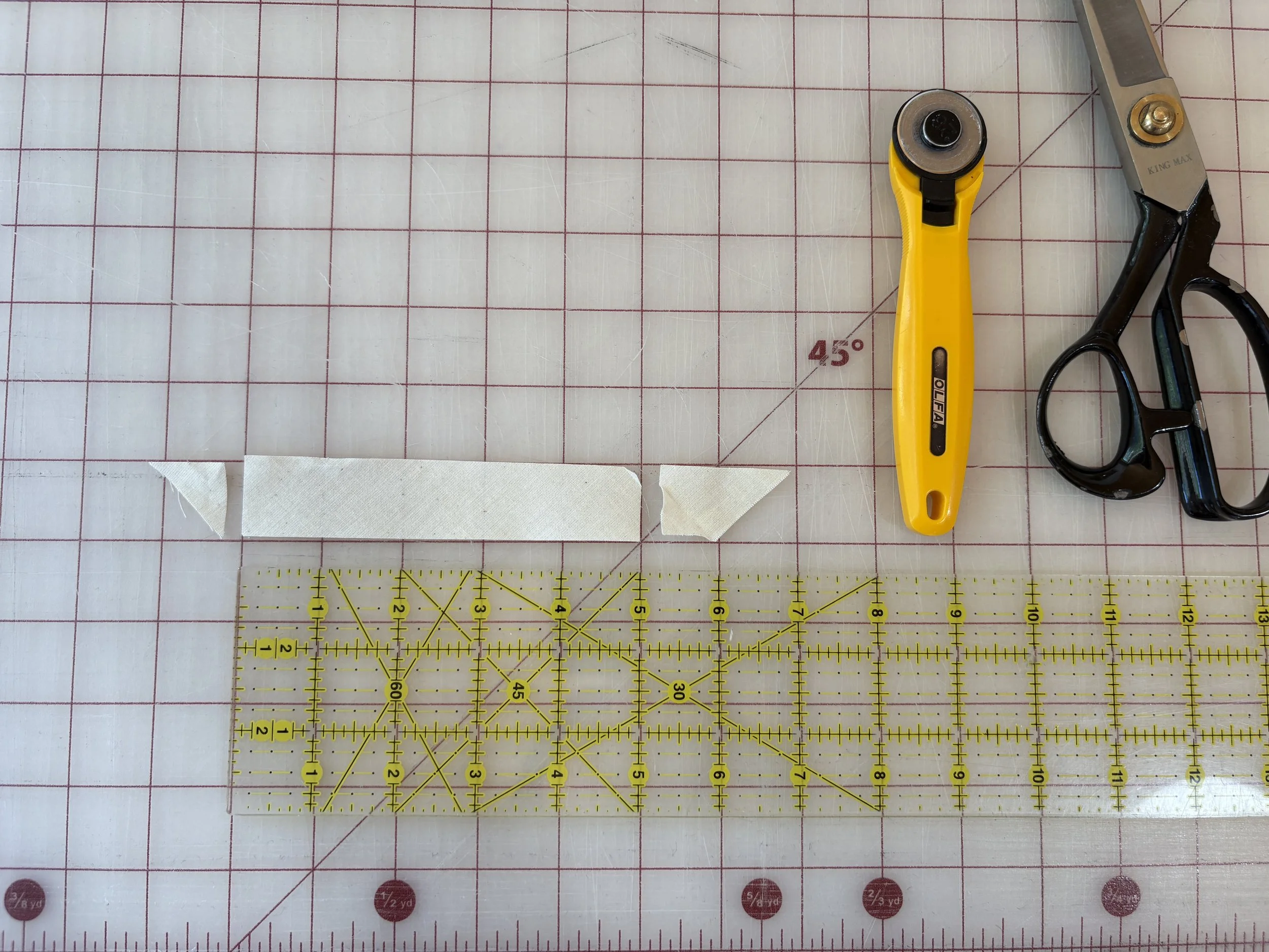 Cut bias strip laid flat on the cutting mat next to a ruler, rotary cutter, and scissors