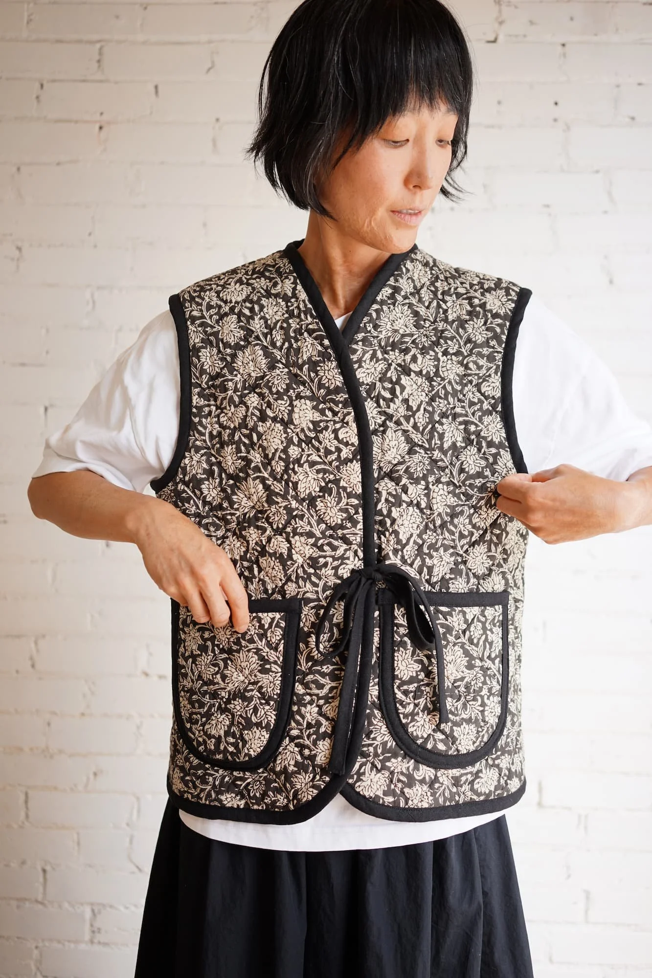 Woman tying closure of block-print quilted Nomad Utility Vest in black and cream floral pattern