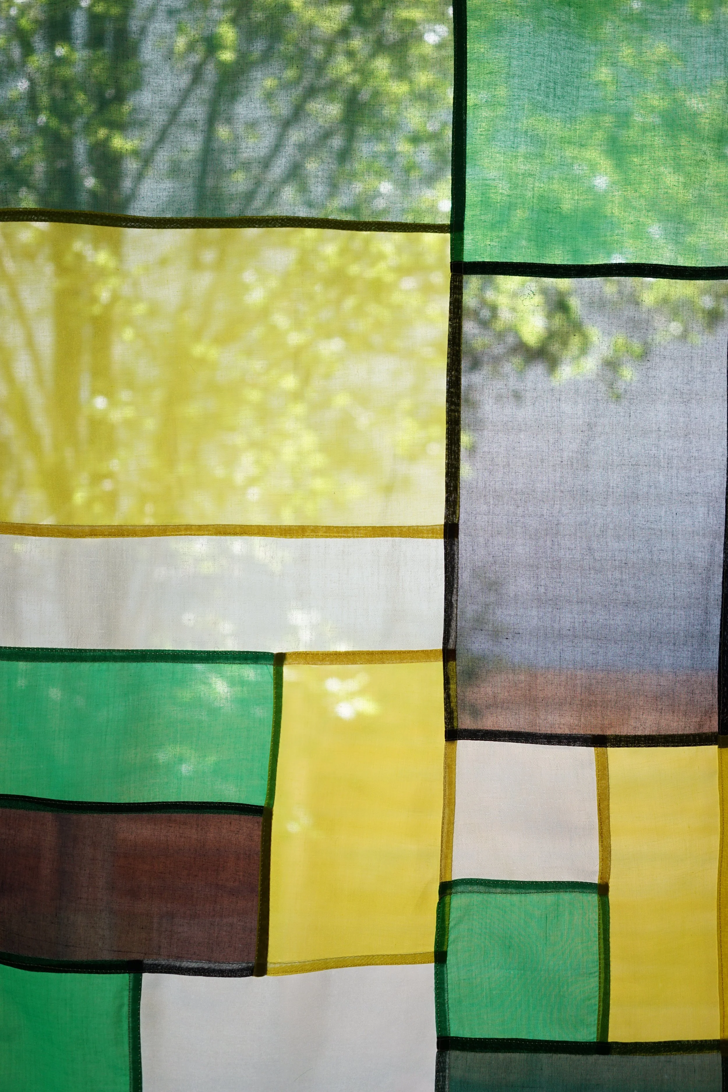 Close-up of citrine jogakbo patchwork showing green, yellow, and gray sheer panels backlit by trees
