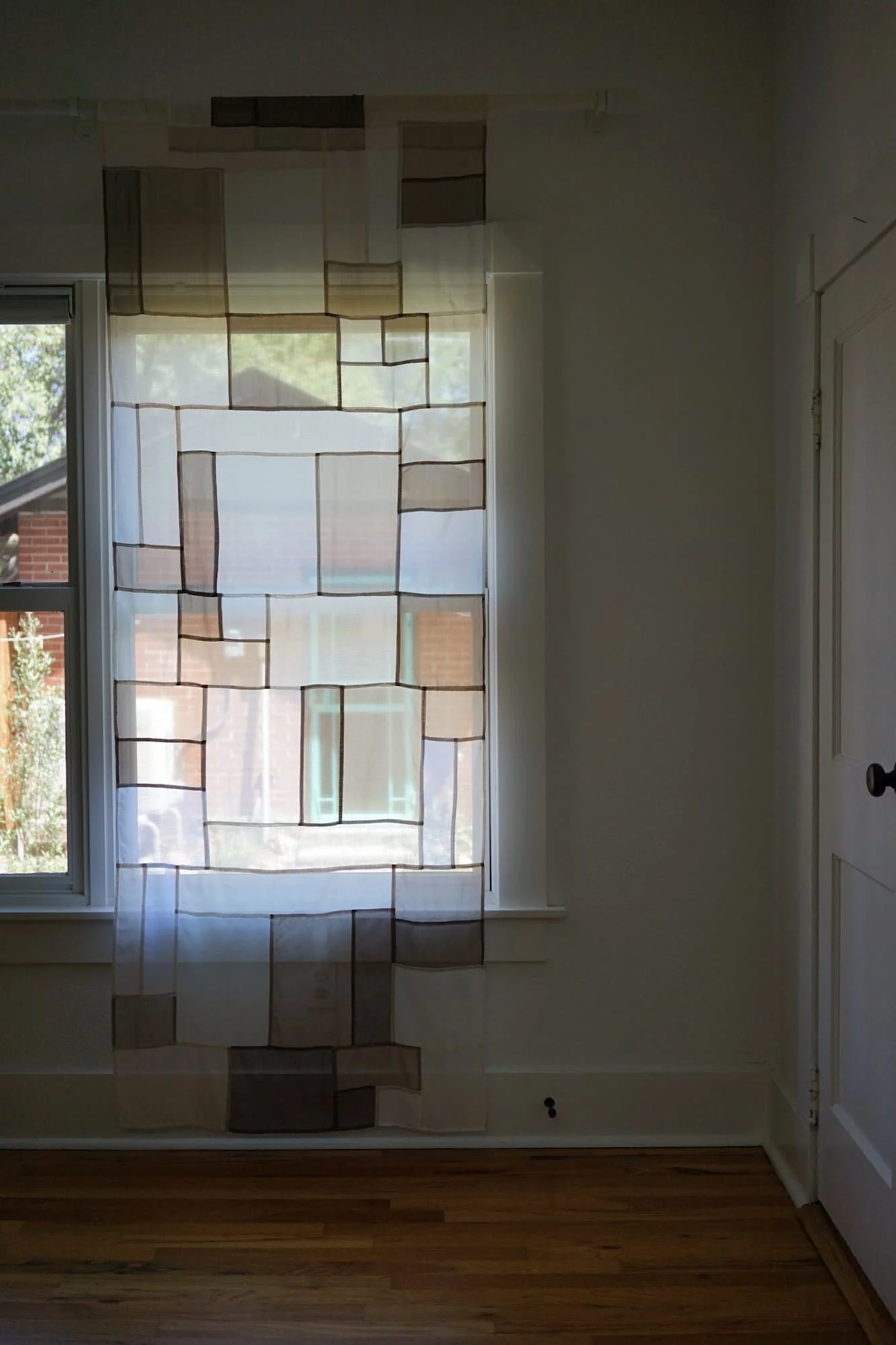 Jogakbo patchwork curtain hanging in dim room, backlit by window