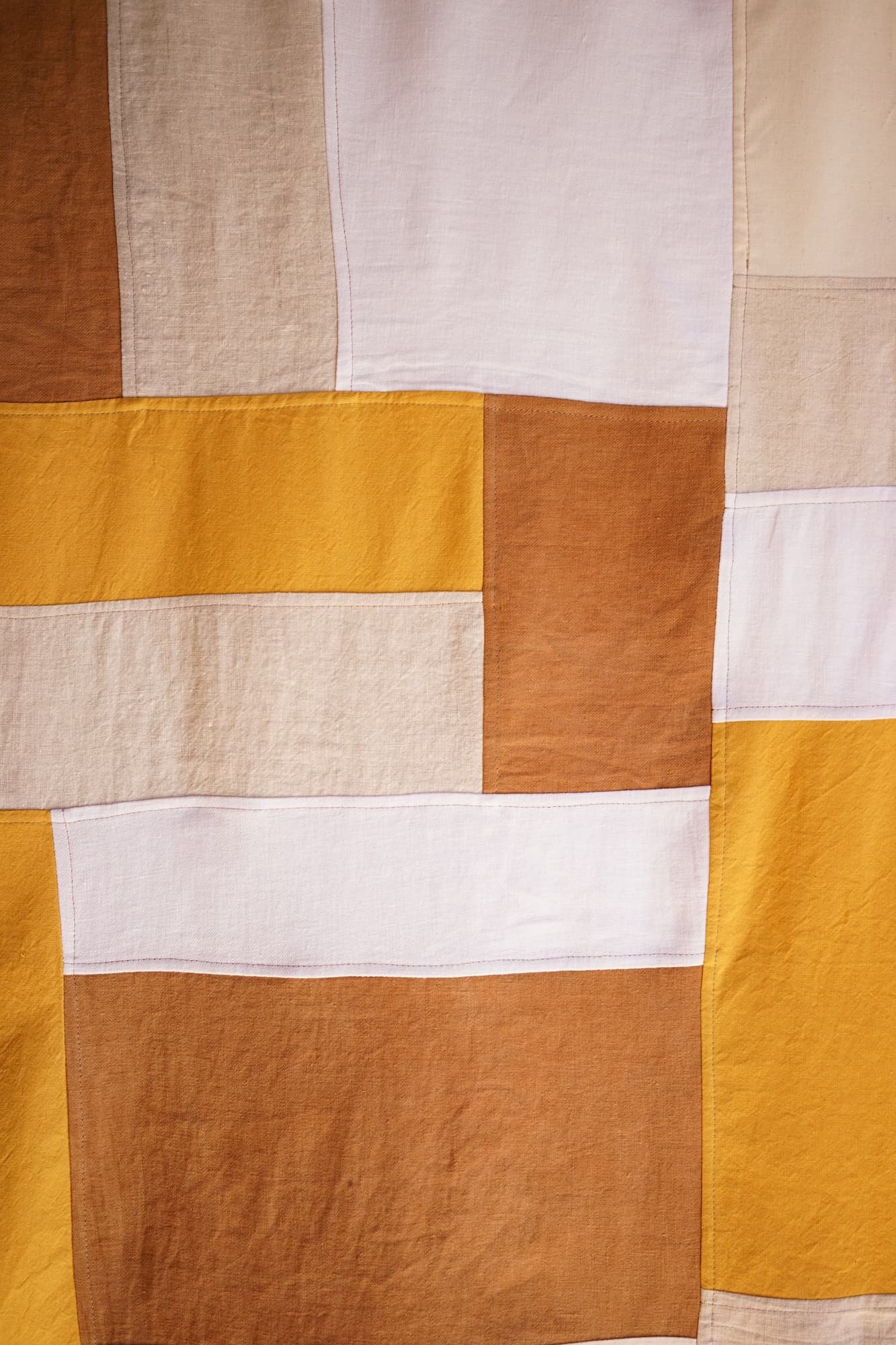 Close-up of amber jogakbo linen patchwork, showing the geometric block piecing and visible stitch lines in mustard, rust, taupe, and white