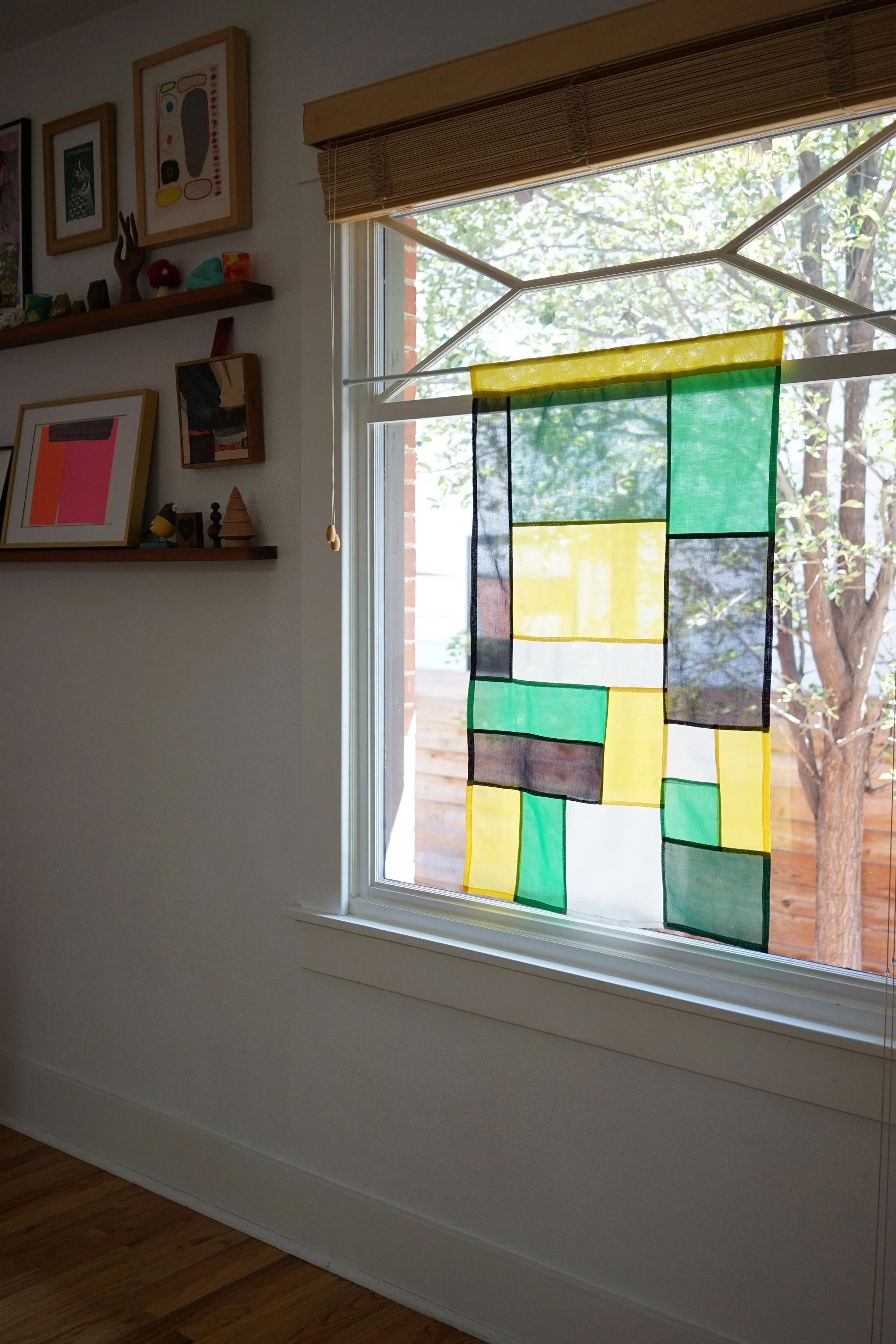 Citrine jogakbo window hanging in living room window with framed art and shelf decor nearby"