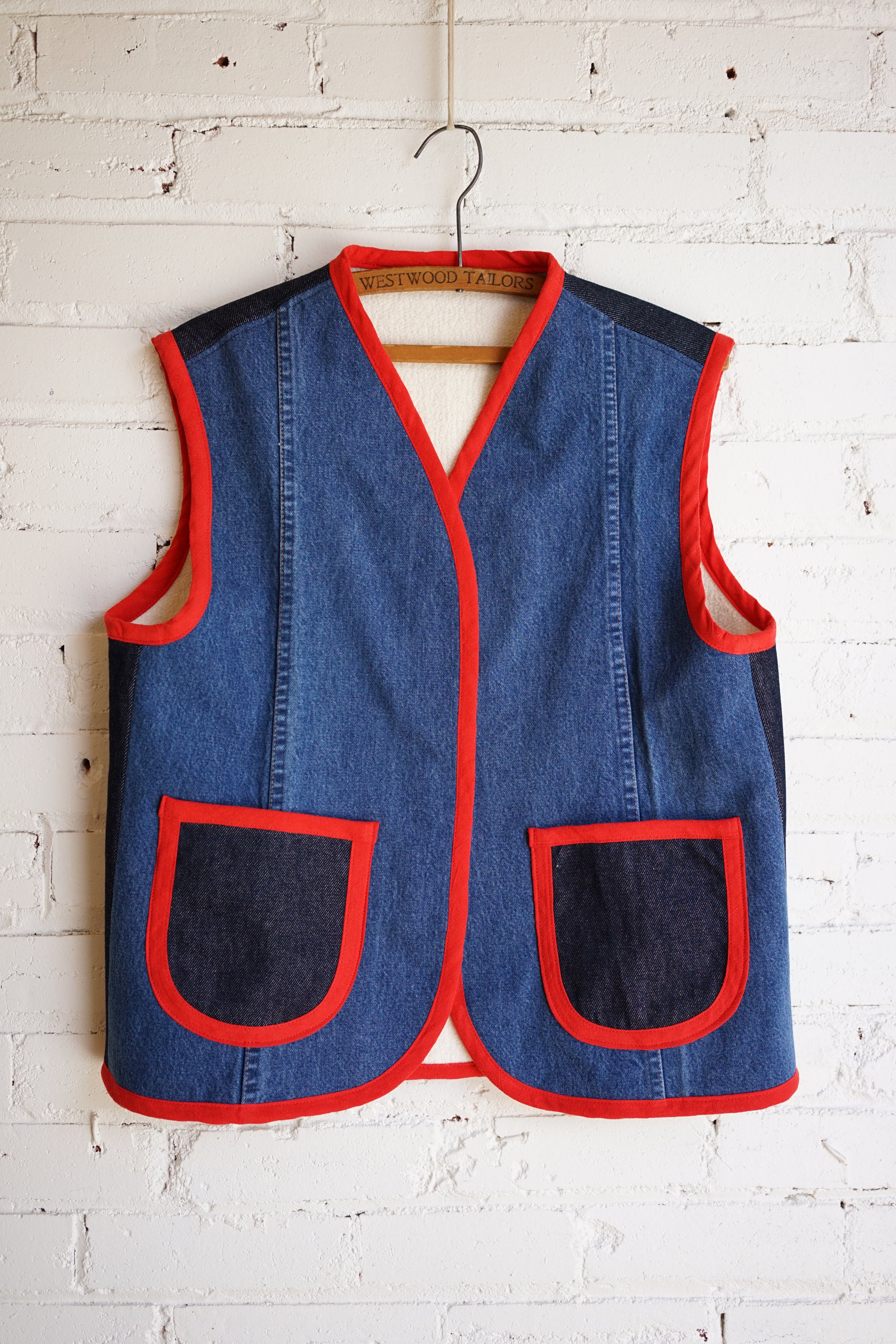 Nomad vest sewing pattern — repurposed denim vest with red bias binding and patch pockets, shown on hanger