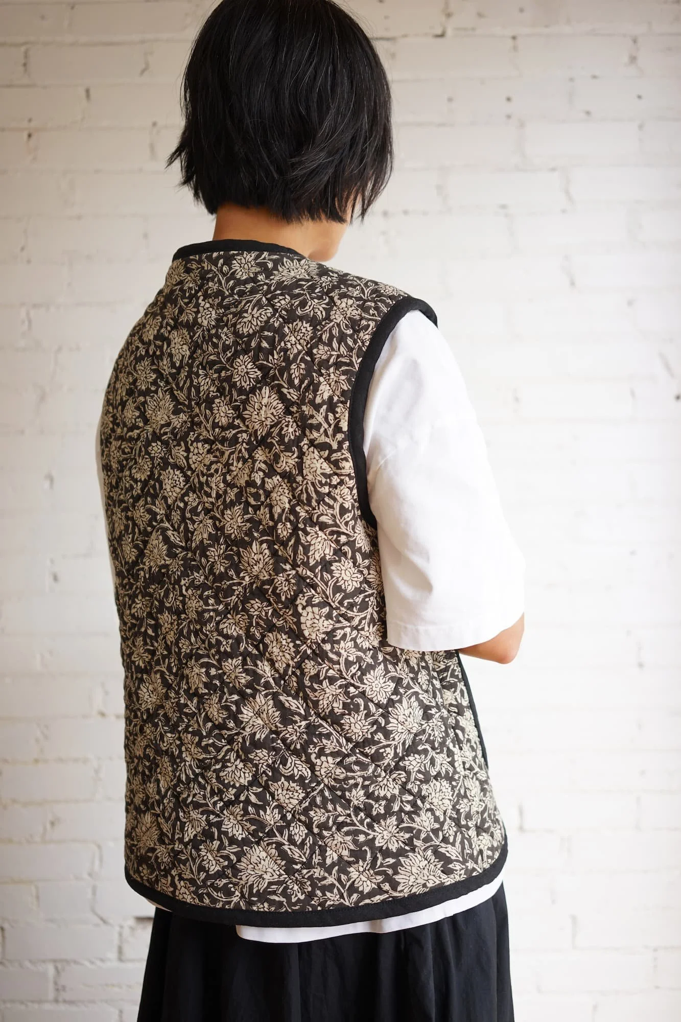 Back view of block-print quilted Nomad Utility Vest in black and cream floral pattern, worn over a white t-shirt