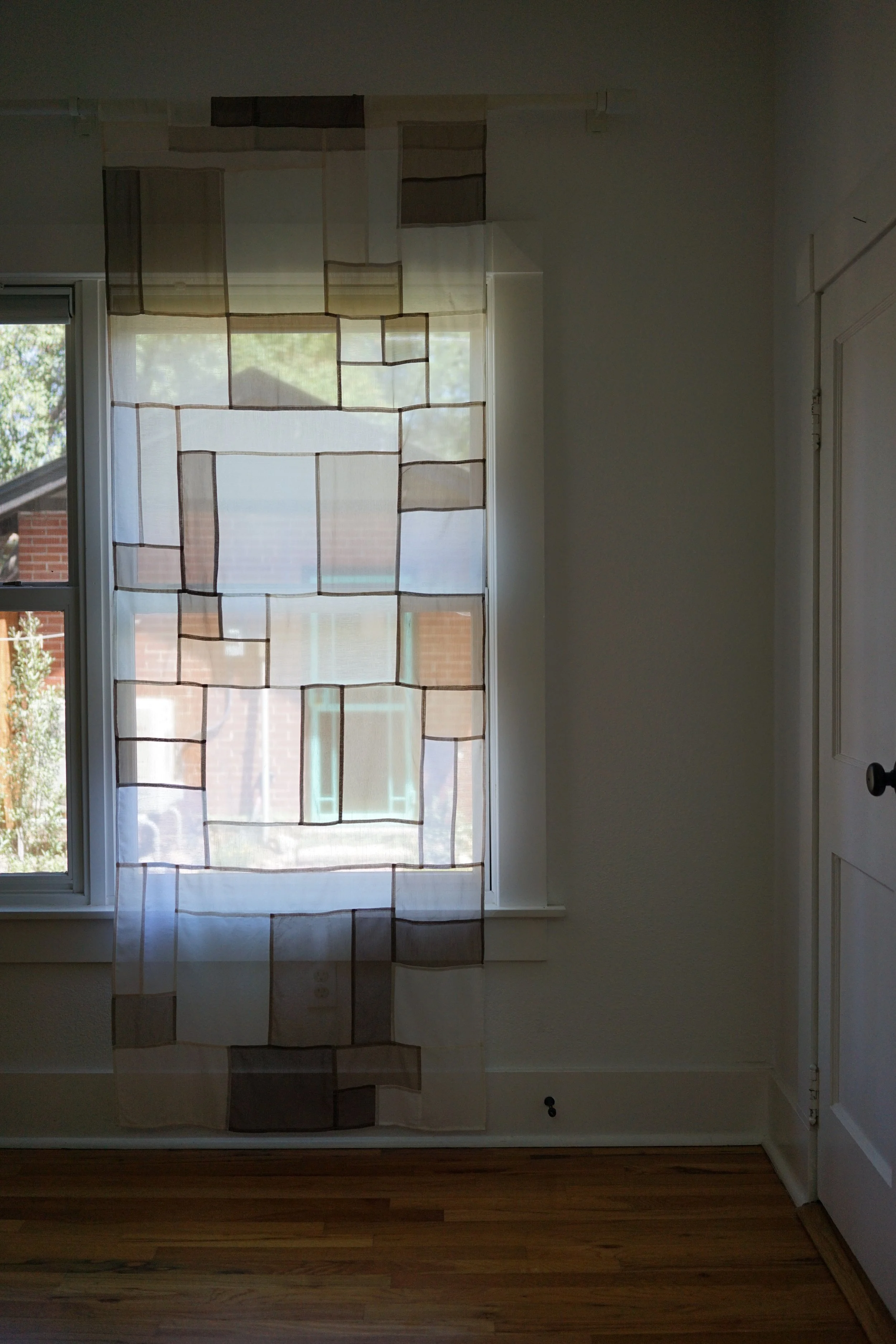 Jogakbo patchwork curtain hanging in dim room, backlit by window