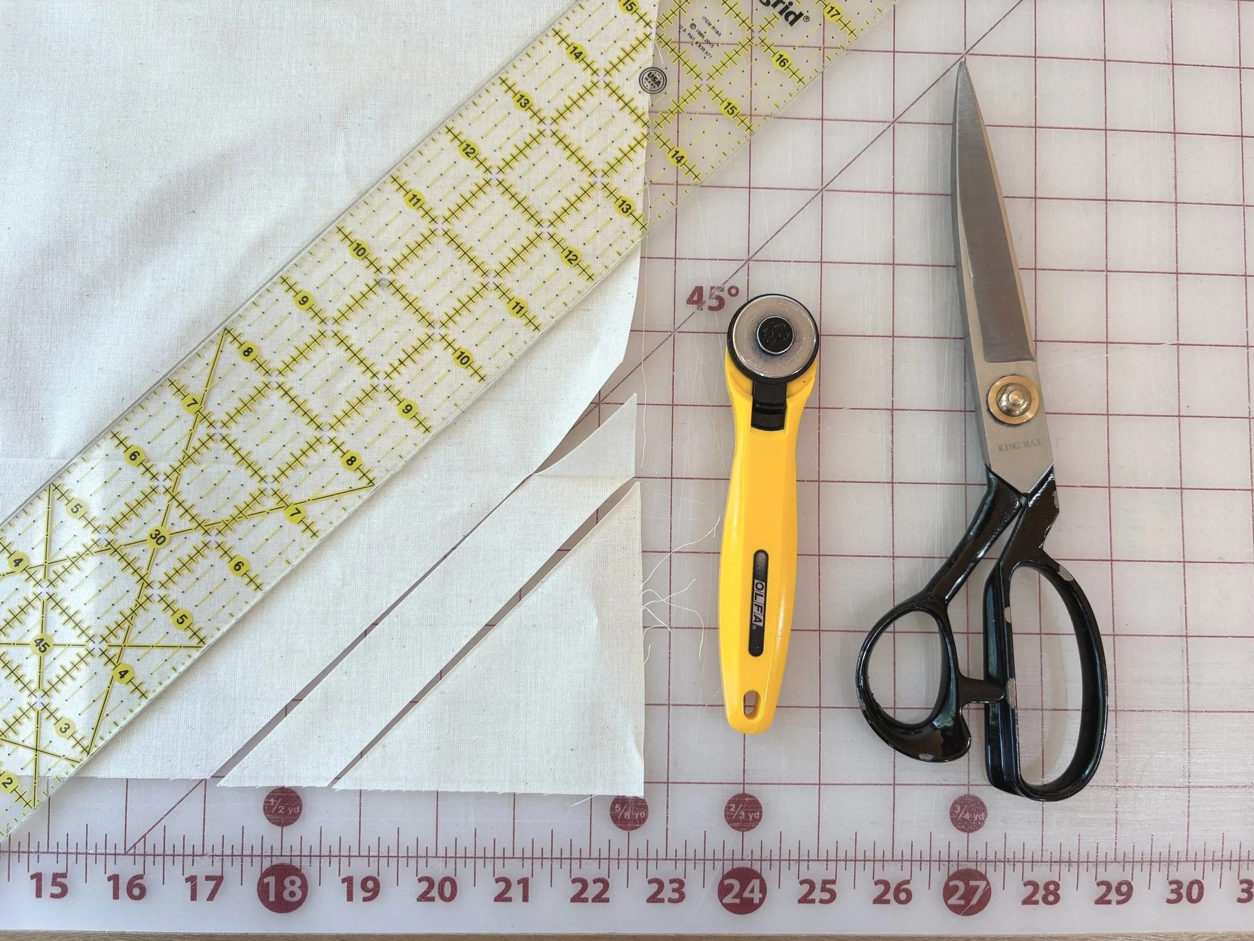 Bias strip cut from fabric on a cutting mat, shown with a rotary cutter and scissors as cutting tool options