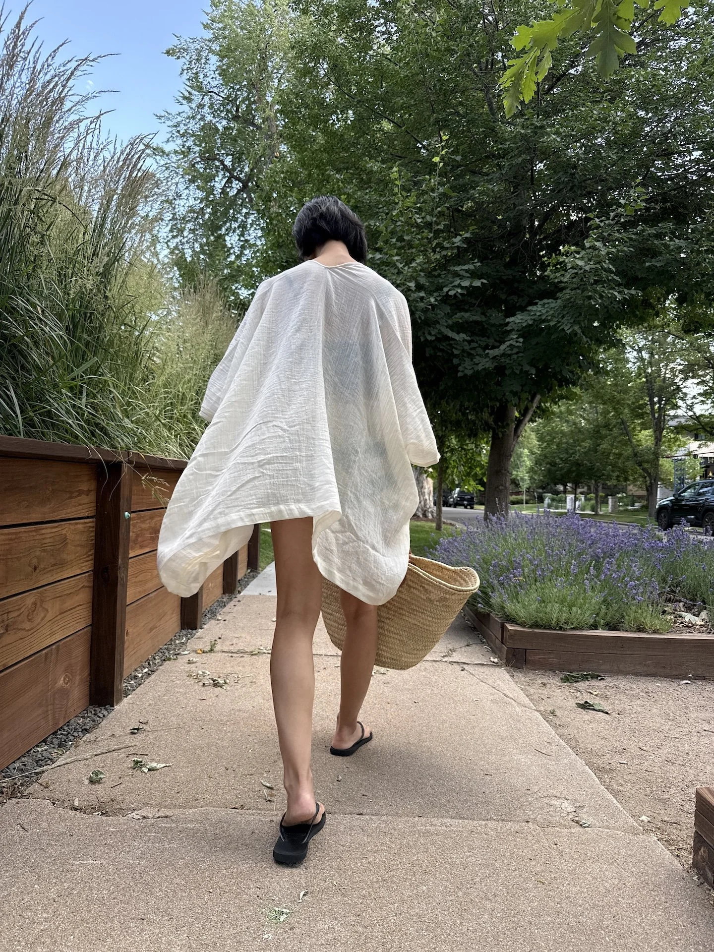 Woman walking away in the short kimono cover-up in white cotton gauze, back view, carrying a woven straw tote bag