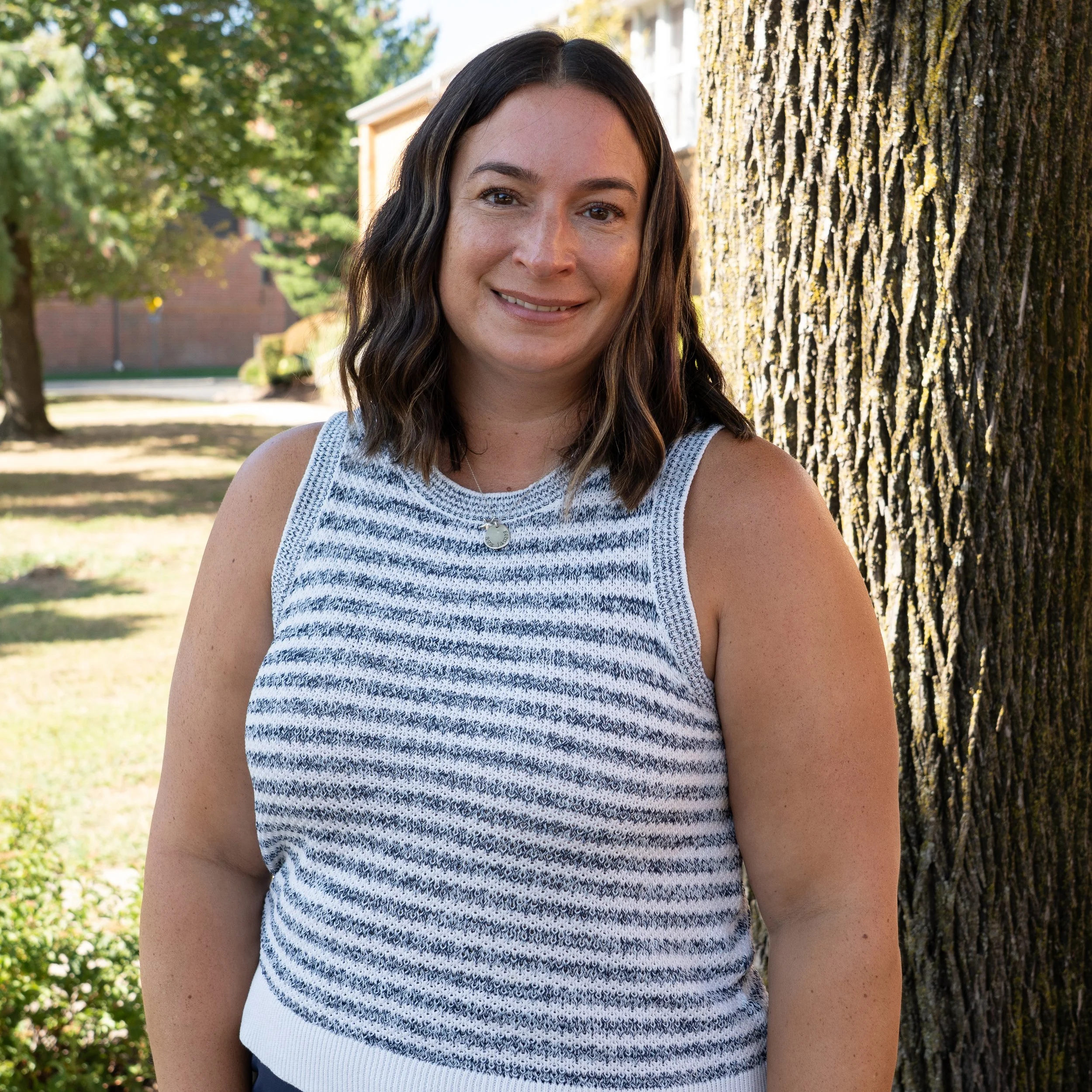 A woman with long brown hair, smiling, wearing a black top, against a gray background.