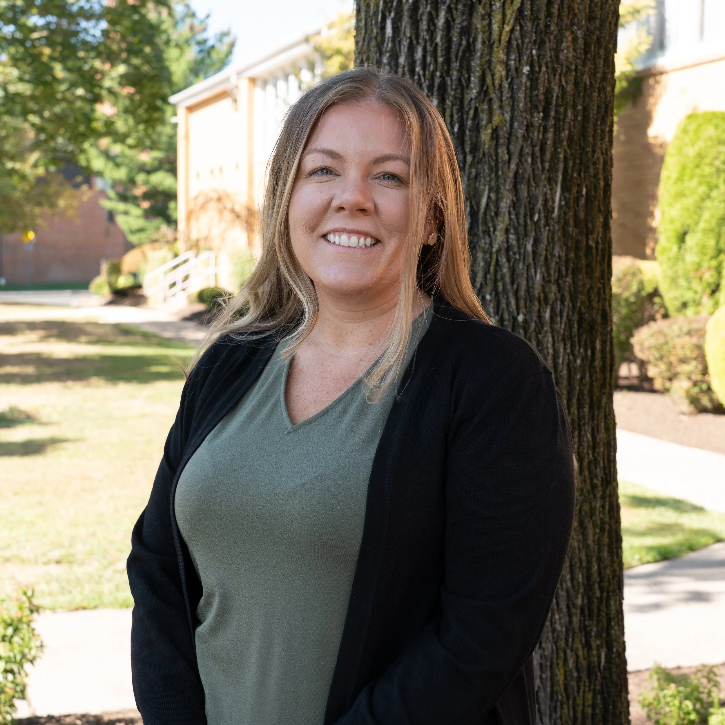 Headshot of a woman with long, wavy blonde hair, smiling, wearing a dark t-shirt with a heart design.