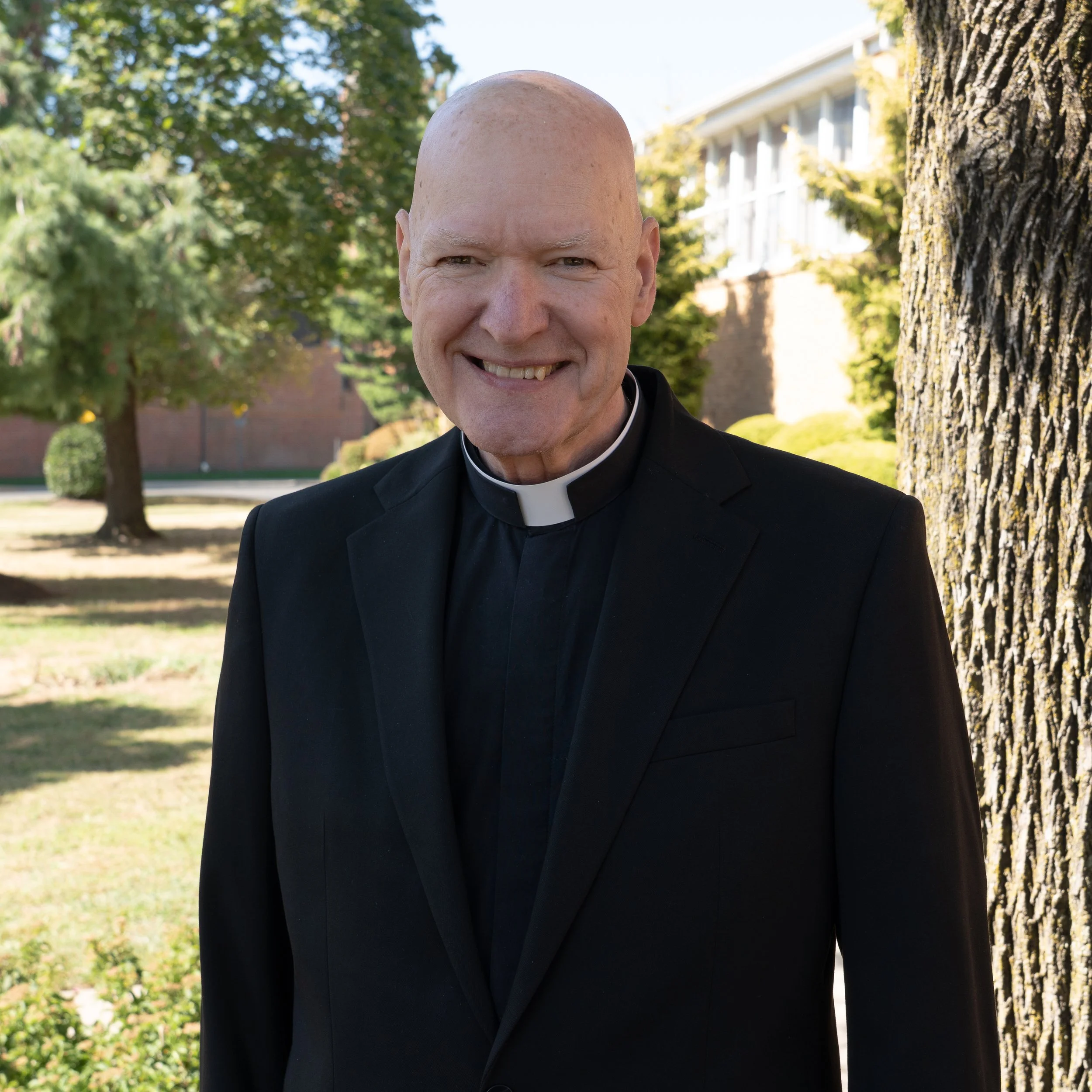 Portrait of a smiling man wearing a black clerical shirt with a white collar.