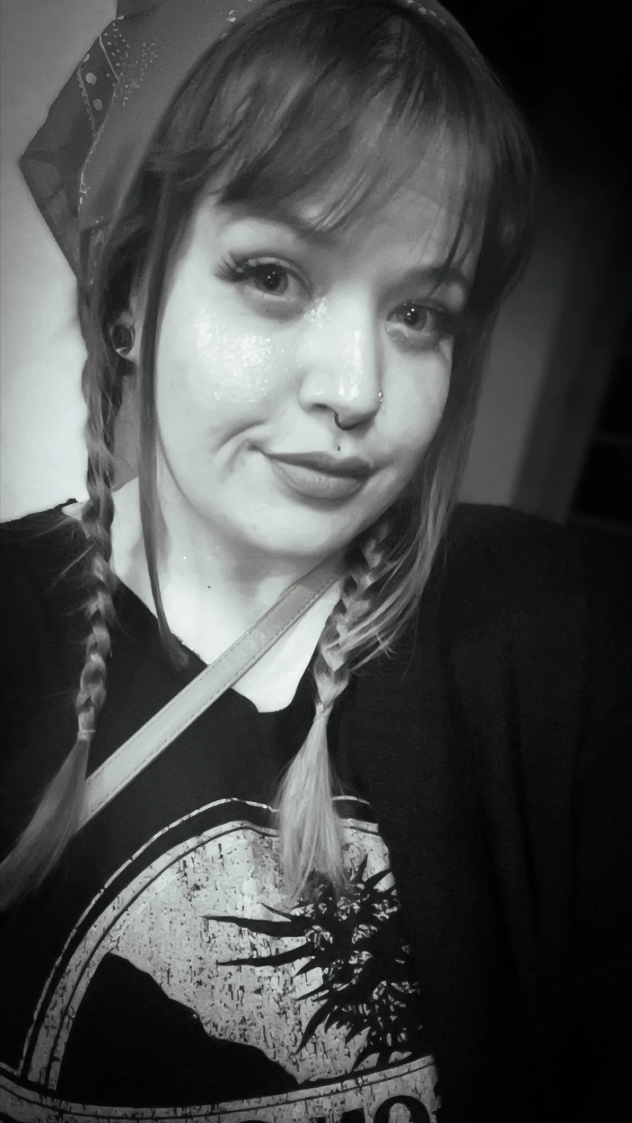 A black and white photo of a young woman with braided hair and a headscarf, wearing a T-shirt with a graphic design.