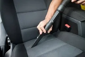 Person using a vacuum to clean the car seat interior.
