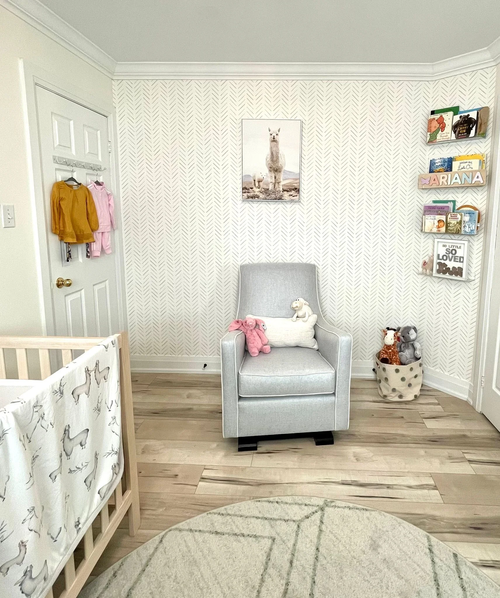 A cozy nursery with a gray armchair, stuffed animals, a crib, and bookshelves on the wall.