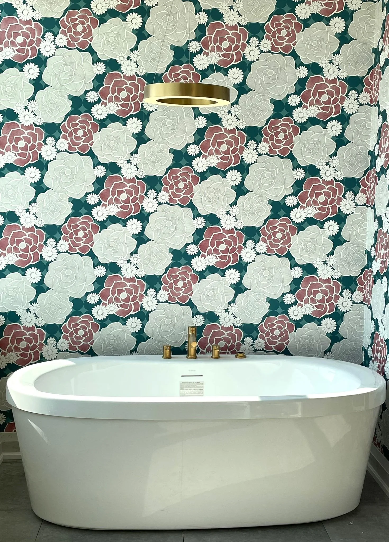 A modern white bathtub with gold fixtures in a bathroom featuring floral-patterned wallpaper with large roses and daisies.