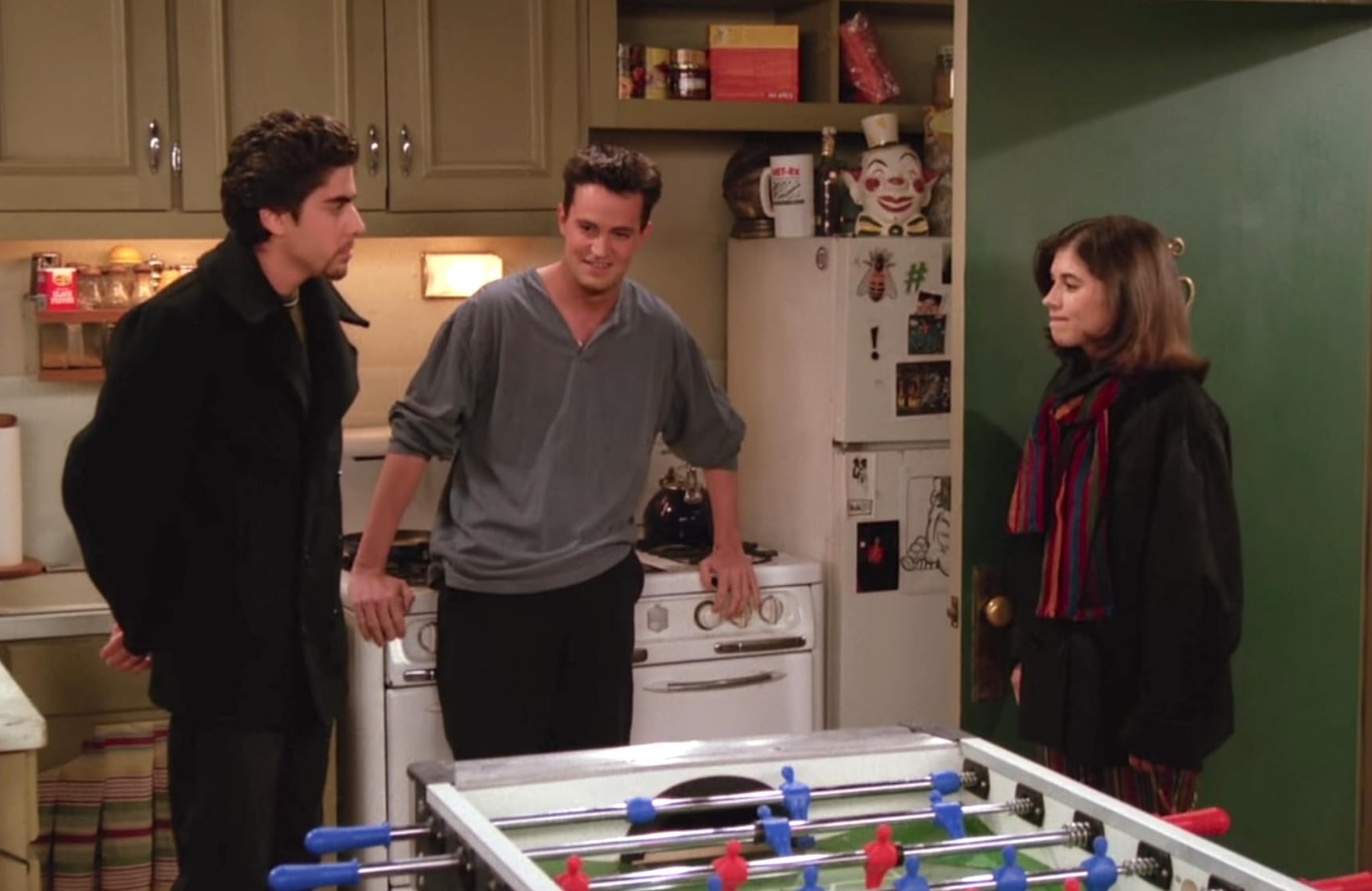 Mary has walked into Joey and Chandlers apartment with a red scarf and big coat on. Chandler is standing between her and Eddie.