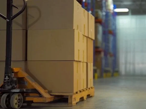 A pallet truck loaded with stacked boxes in a warehouse, representing a dedicated pallet delivery service.