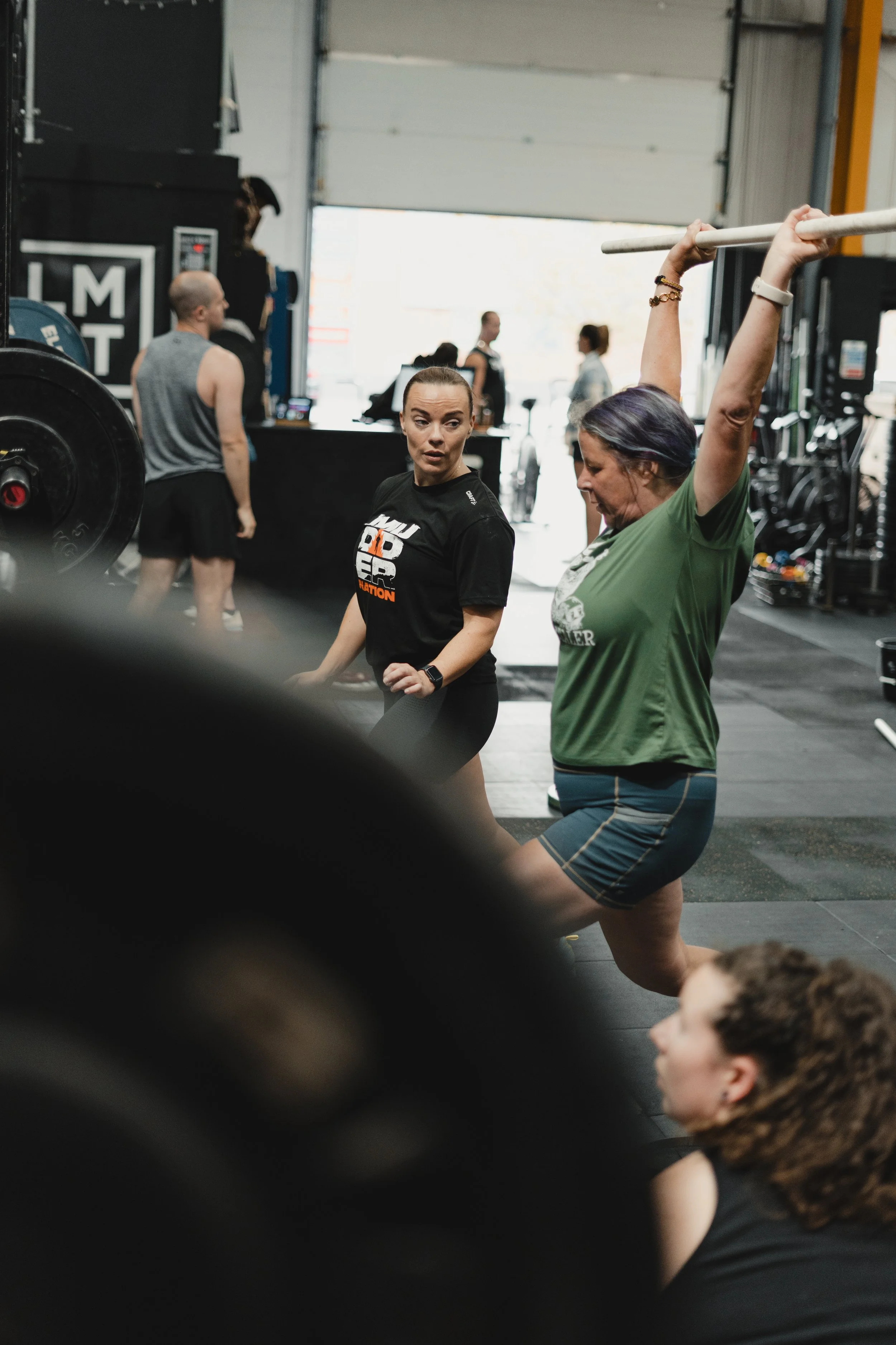 A woman lifts a barbell above her head in an Olympic Weightlifting class