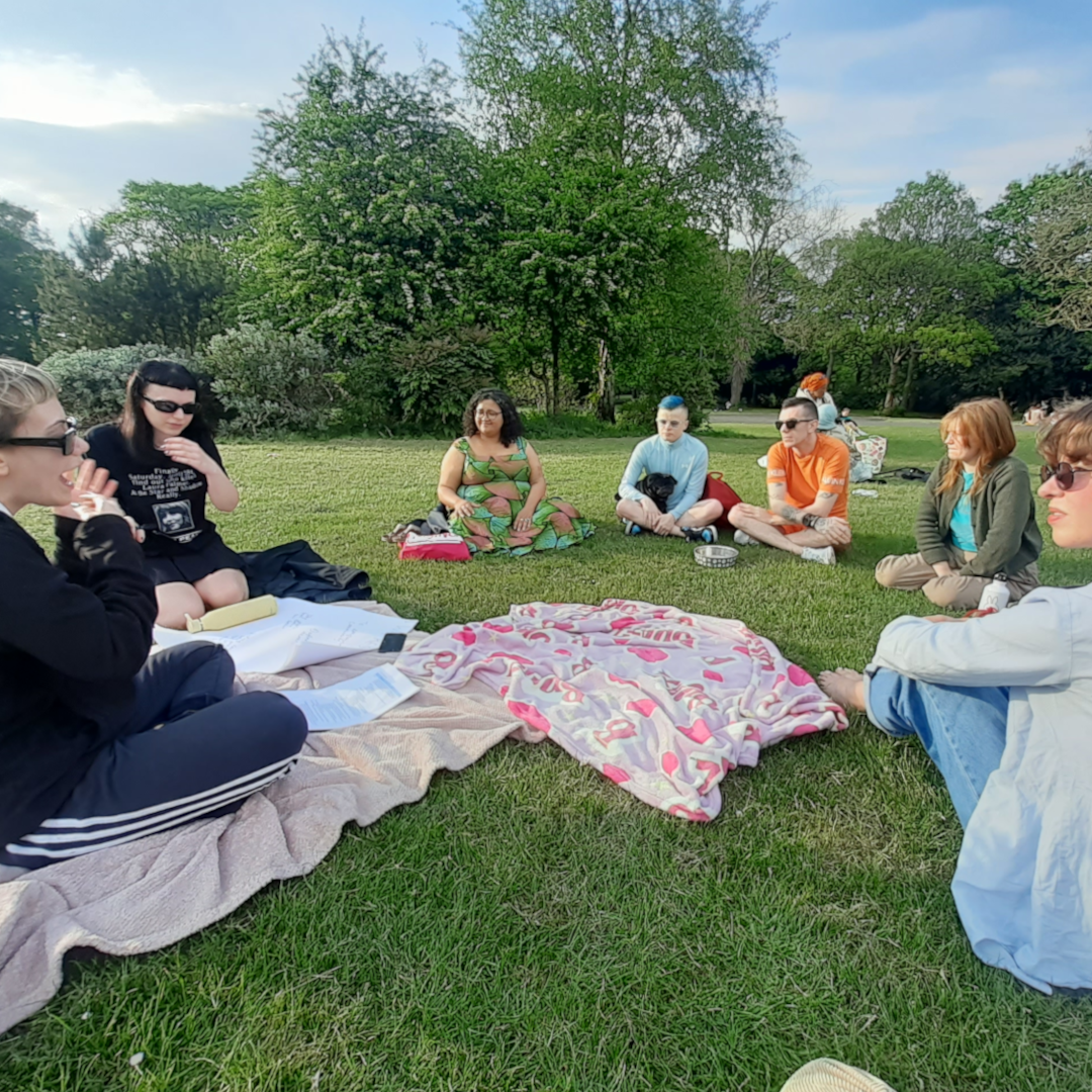 Two participants sit close together in the grass, studying eviction resistance handouts. One takes notes while the other holds a colourful worksheet.