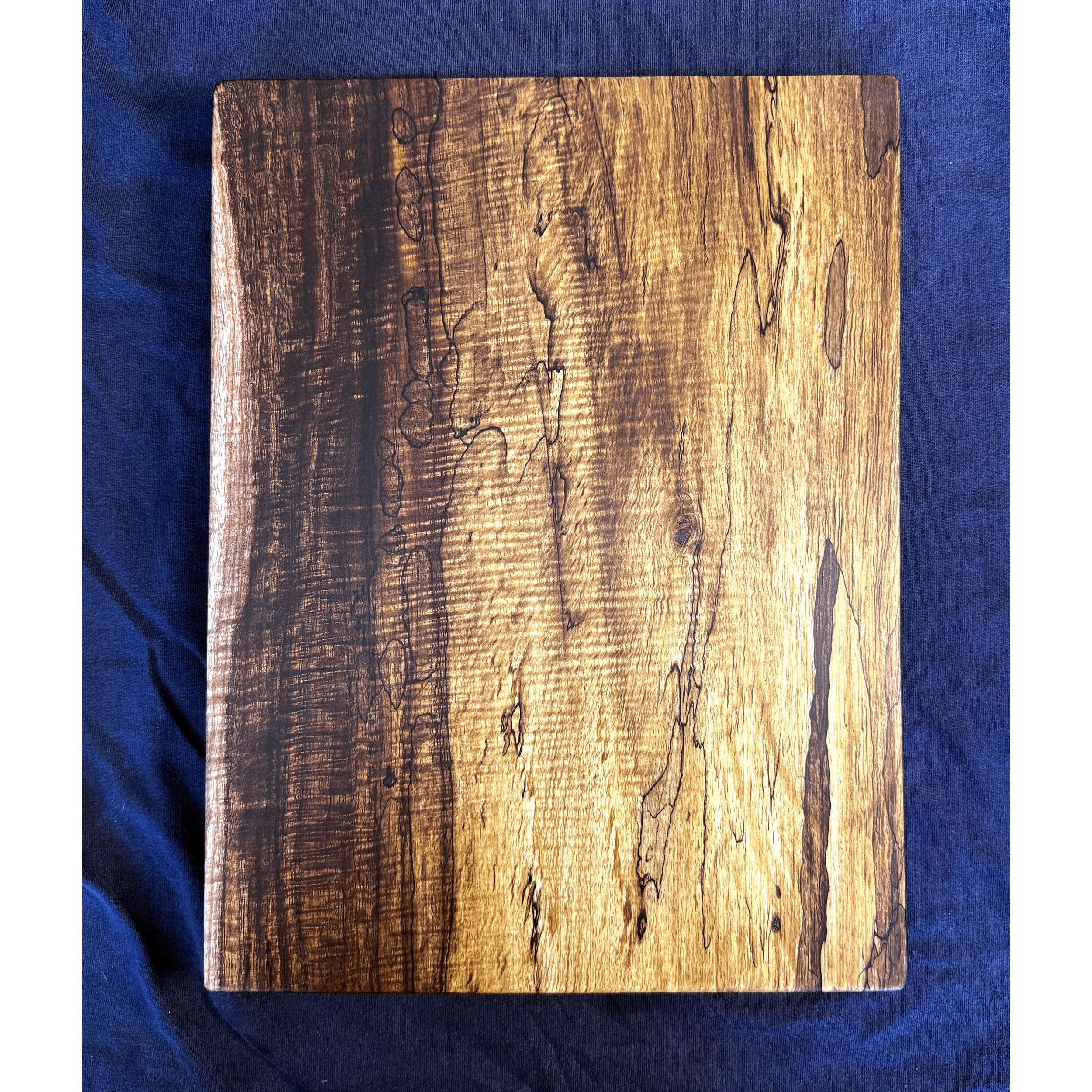 Simple charcuterie board, 9" x 12" x 3/4", 2024. Made of spalted Koa and finished with food grade oil/beeswax finish. This piece of Hawaiian Koa exhibits several qualities. The warm tones, and a beautiful "curl" appreciated by musical instrument and 