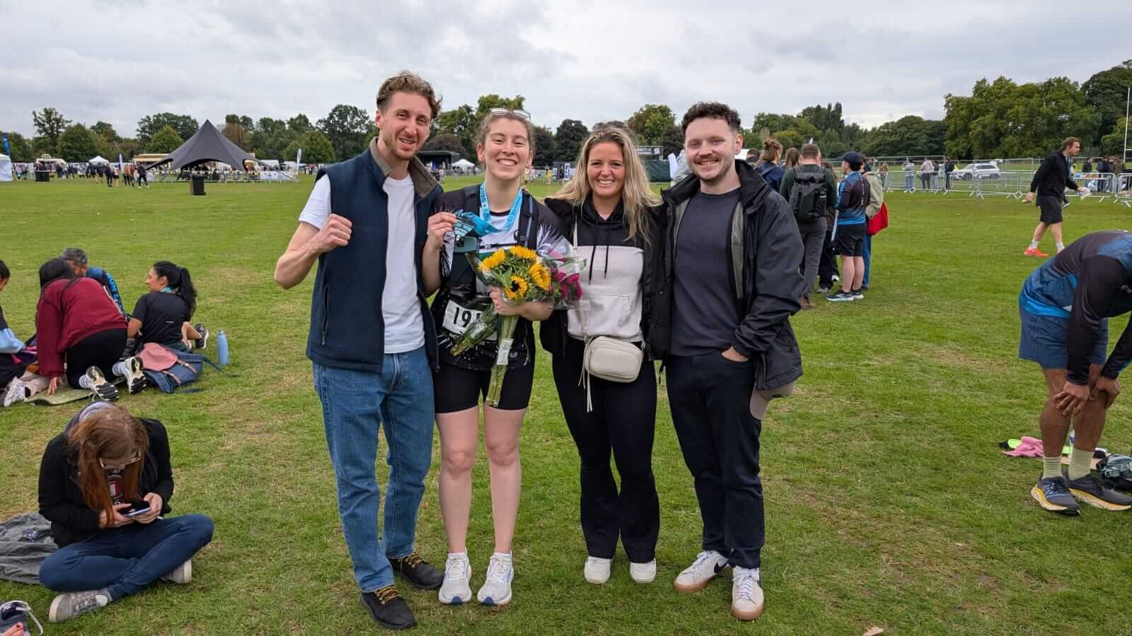 Freya at the finish line holding a bunch of sunflowers and her medal, alongside three friends from running club