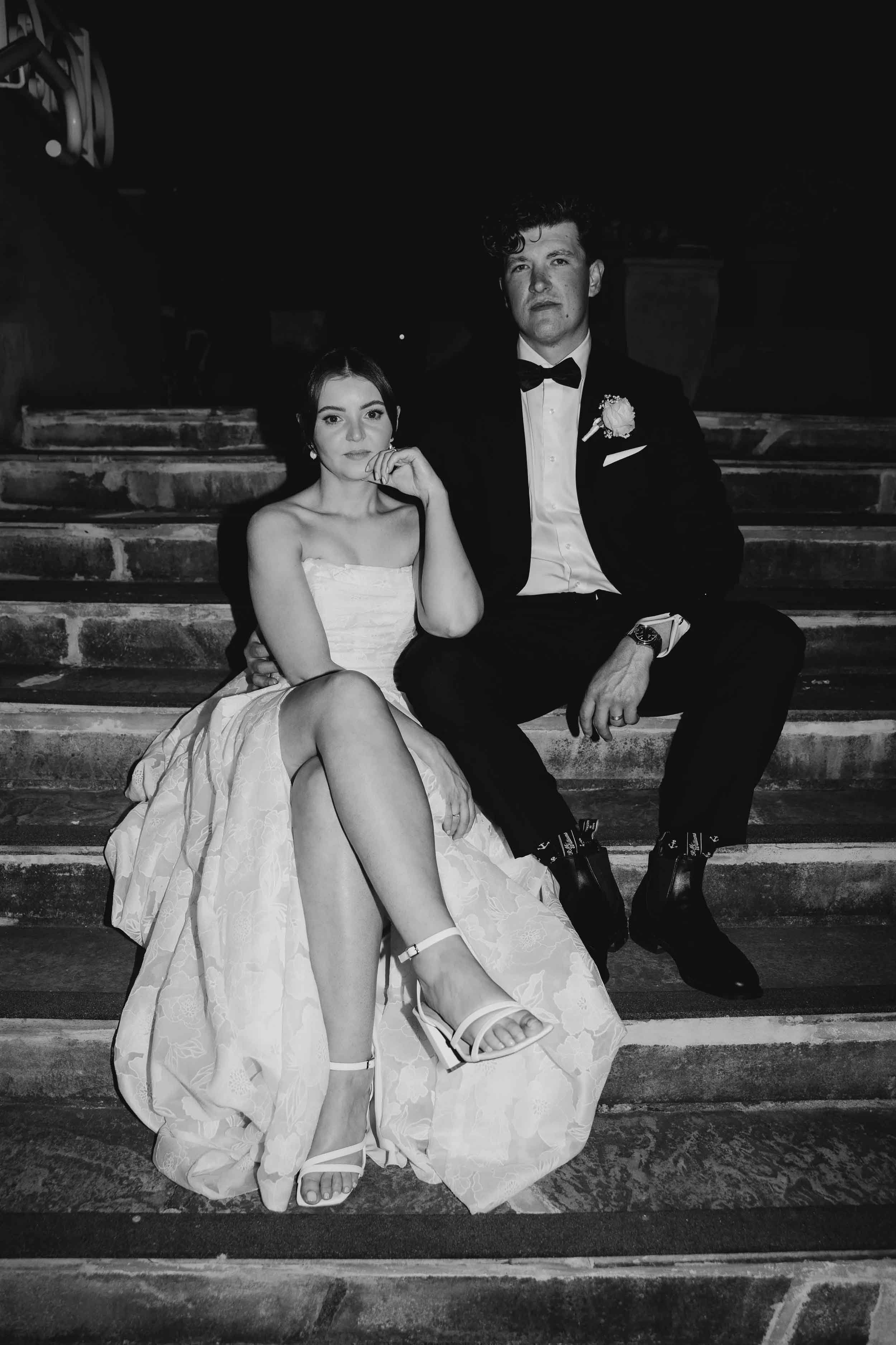 In black and white, Amanda and Jesse sit close on the heritage stone steps at Farm Vigano, her gown spilling down the stairs.