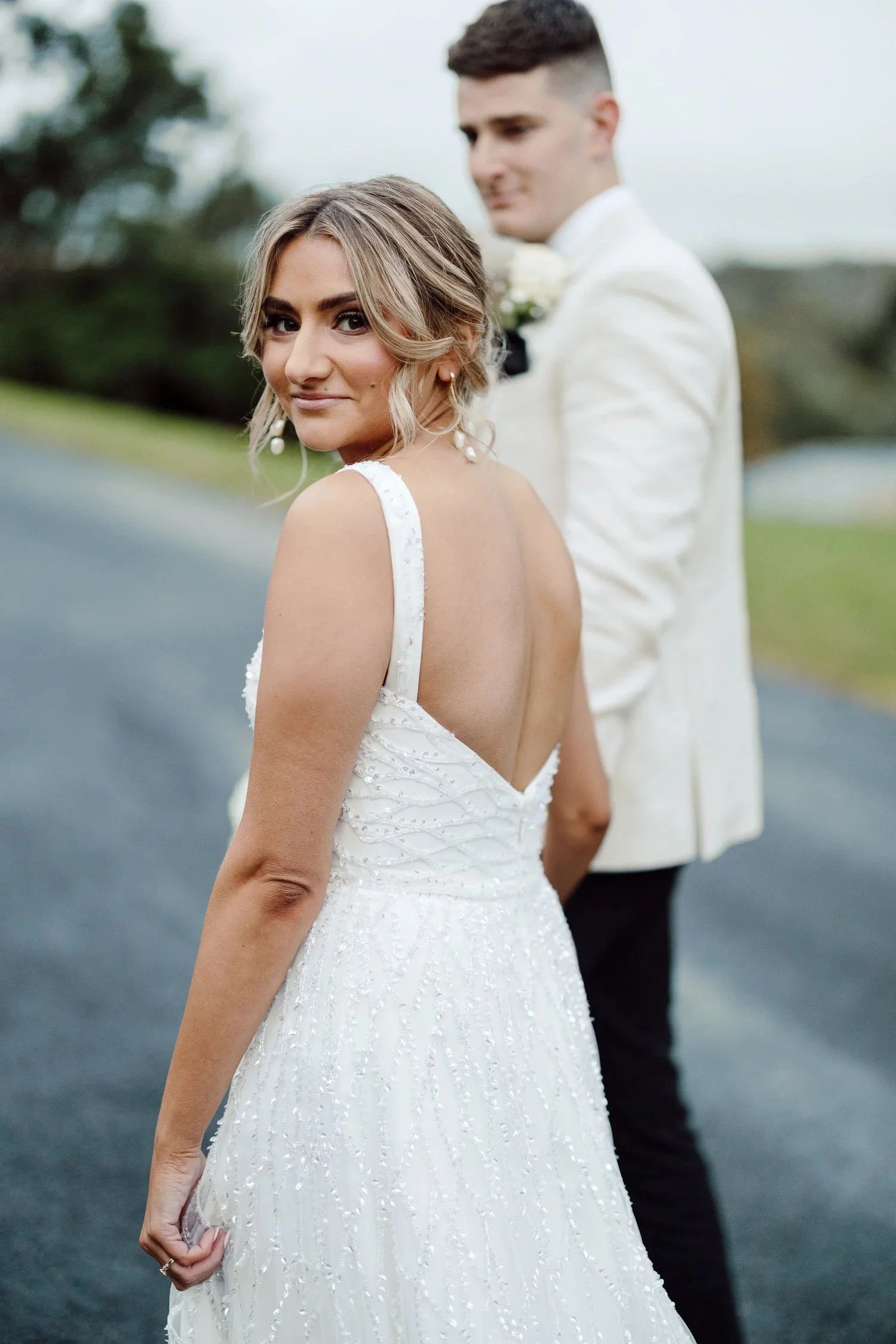 Nicola looks back over her shoulder in her beaded Anna Campbell gown, Nick blurred behind her on the drive at Bramleigh Estate.