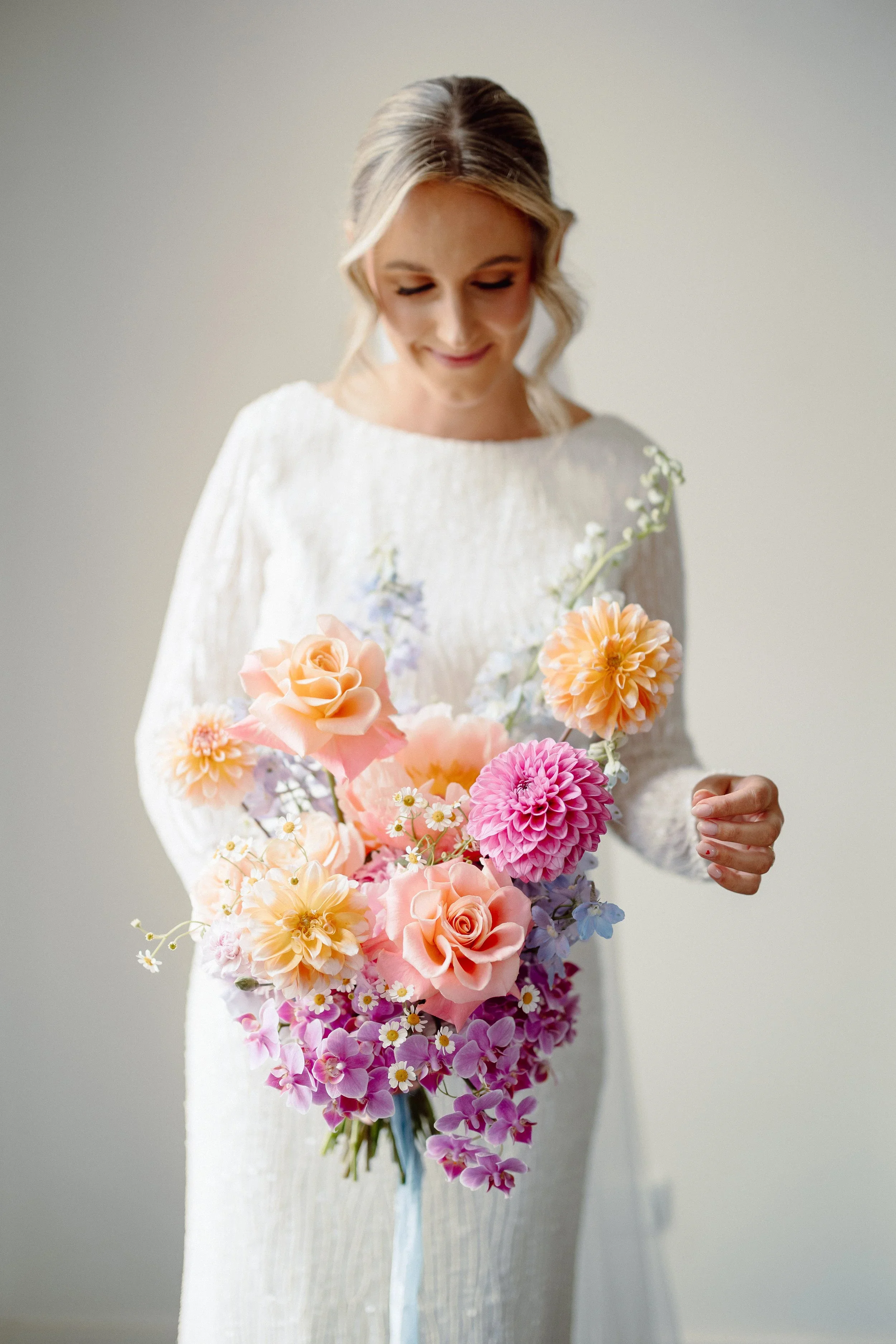 Aisling looks down at her bouquet of peach roses, pink dahlias, purple orchids and daisies, a pale blue ribbon falling from the stems.