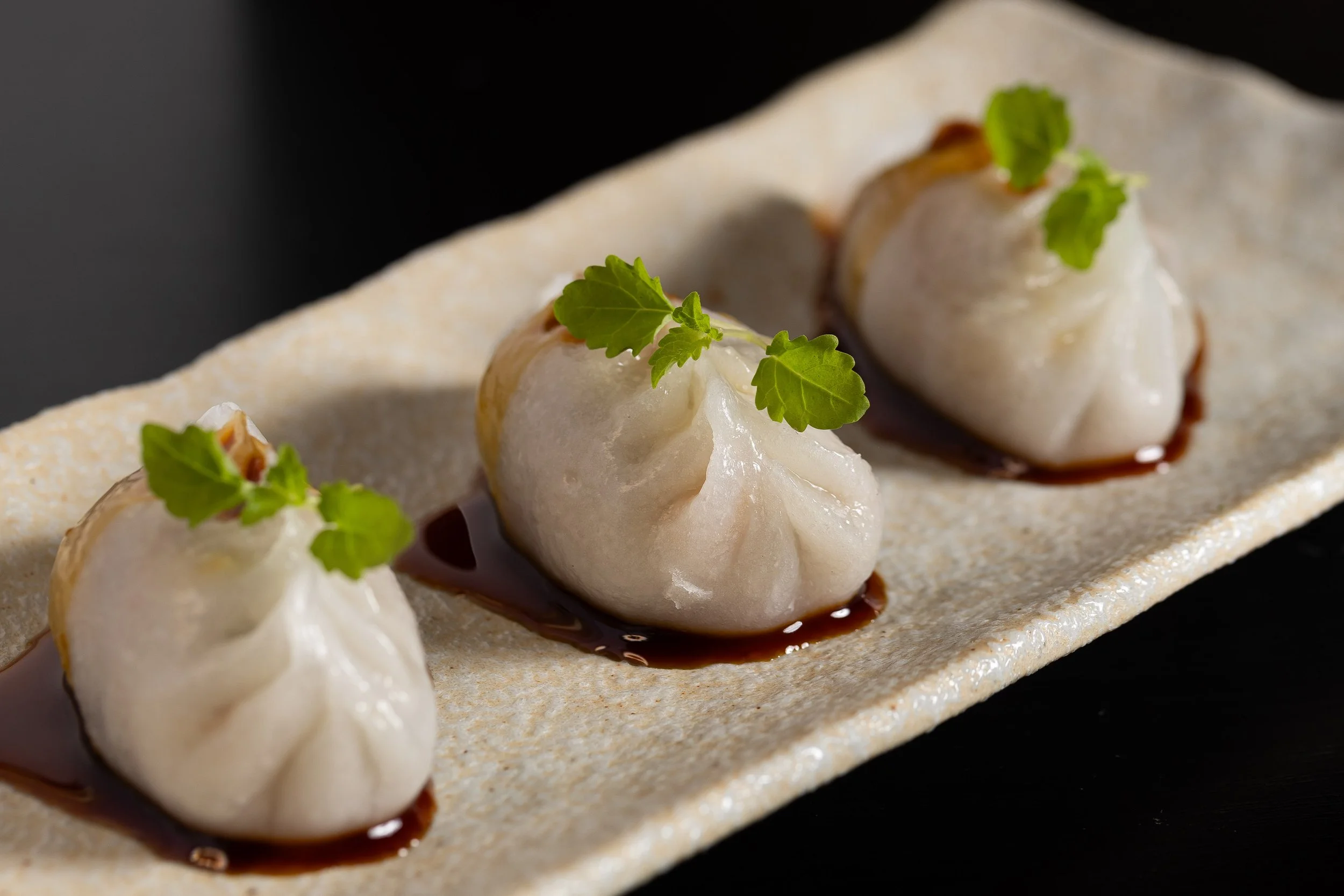 Three dumplings garnished with green herbs on a rectangular plate with a dark background.