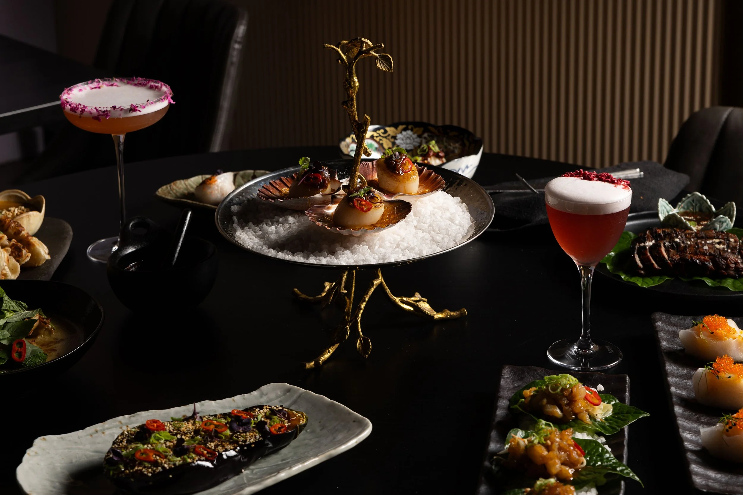 Elegant table with assorted gourmet dishes and cocktails, featuring seafood, appetizers, and drinks with a dark background.
