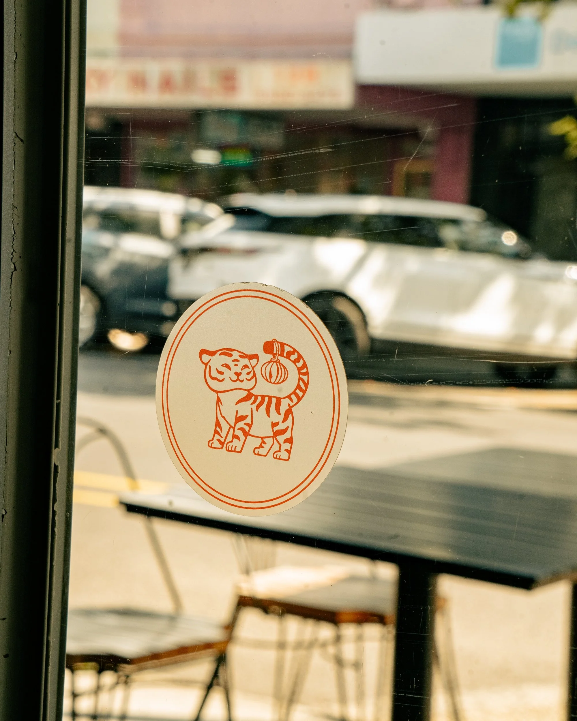 A sticker of a cartoon tiger holding a traditional Chinese lantern is on a glass door, with a blurry street scene in the background.