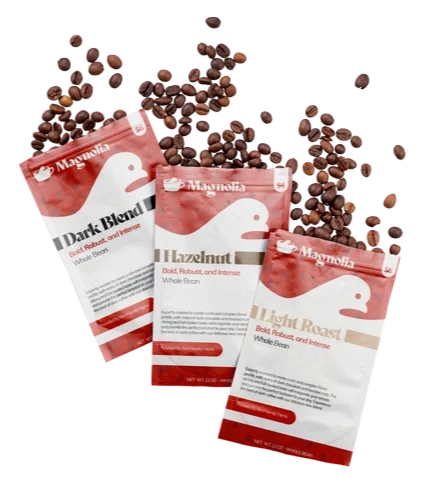 Three bags of Magnolia coffee beans with scattered coffee beans around them.